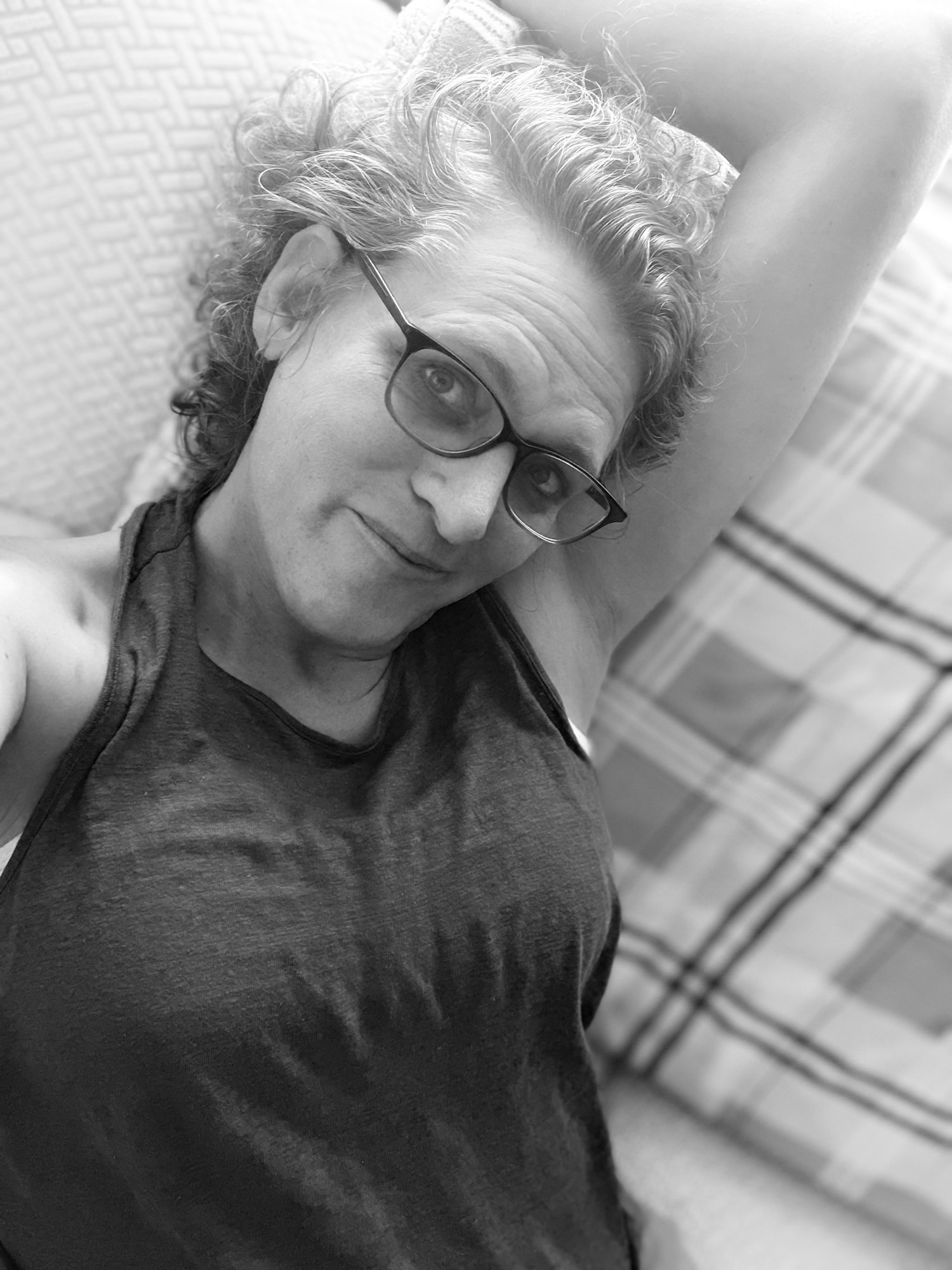 monochrome: emily laying on a sofa in a tank top, one arm seductively behind her head, a knowing smile on her face, flirting for compliments