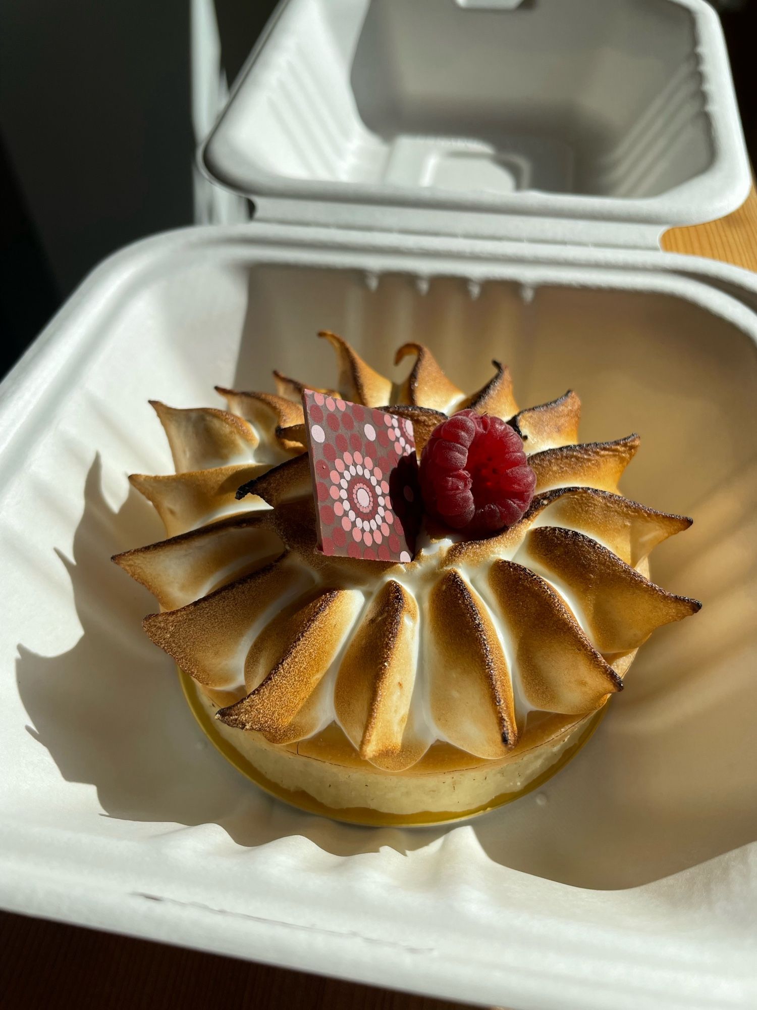 Photo of a small tart with perfect meringue, a raspberry, and decorative chocolate square on top