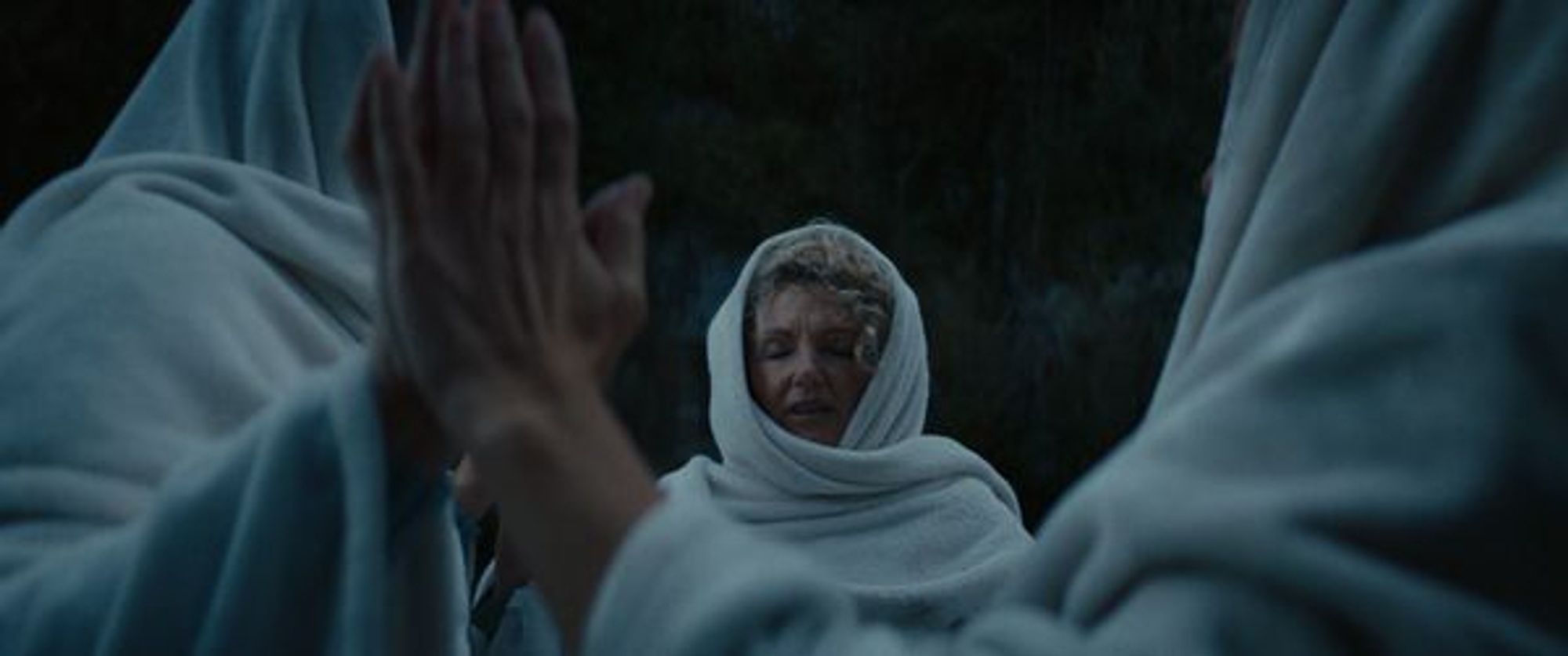 A sill from the film Shadowland. Three white women in long, hooded white robes stand with their hands raised and pressed together, with thick foliage in the background.