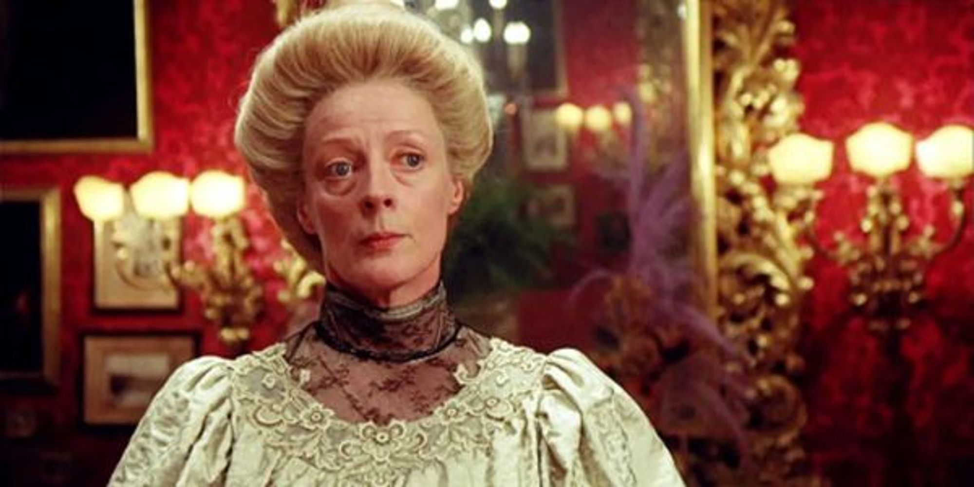 A still from the film A Room With A View. A middle-aged white woman in elegant early 20th Century aristocratic clothing sits in a room with expensive red wallpaper and gold candelabras, looking serenely unimpressed.