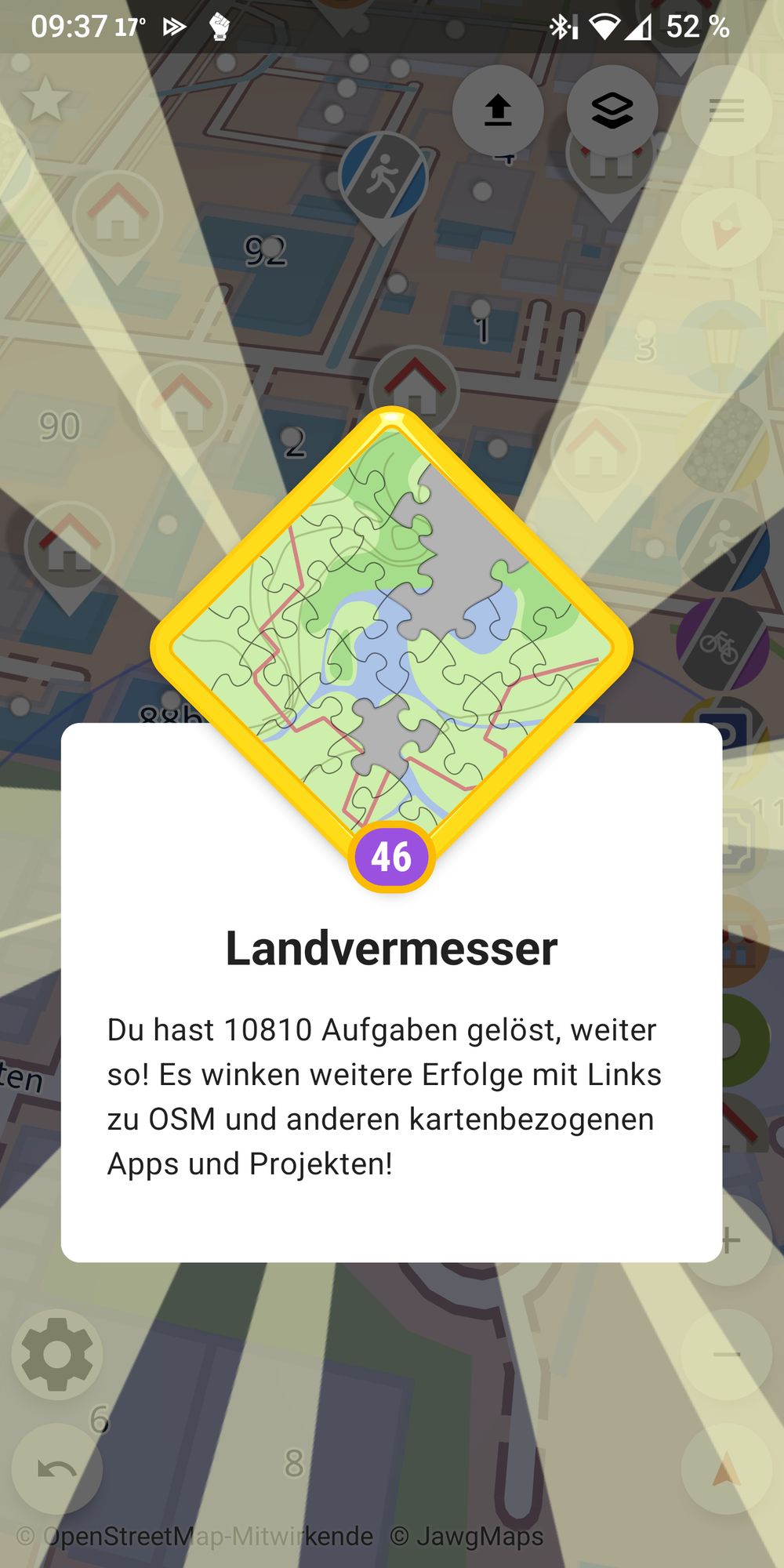 Das Bild zeigt einen Screenshot der App StreetComplete. Im Vordergrund wird ein Erfolg namens "Landvermesser" angezeigt. Der Nutzer hat 10.810 Aufgaben gelöst und erhält die Aufforderung, weiterzumachen, um weitere Erfolge zu erreichen. Der Text hebt hervor, dass Links zu OSM (OpenStreetMap) und anderen kartenbezogenen Projekten und Apps bereitstehen. Im Hintergrund ist eine Karte mit verschiedenen Symbolen und Markierungen zu sehen, die auf Punkte oder Aufgaben hinweisen, die mit der OpenStreetMap-Datenbank verknüpft sind.