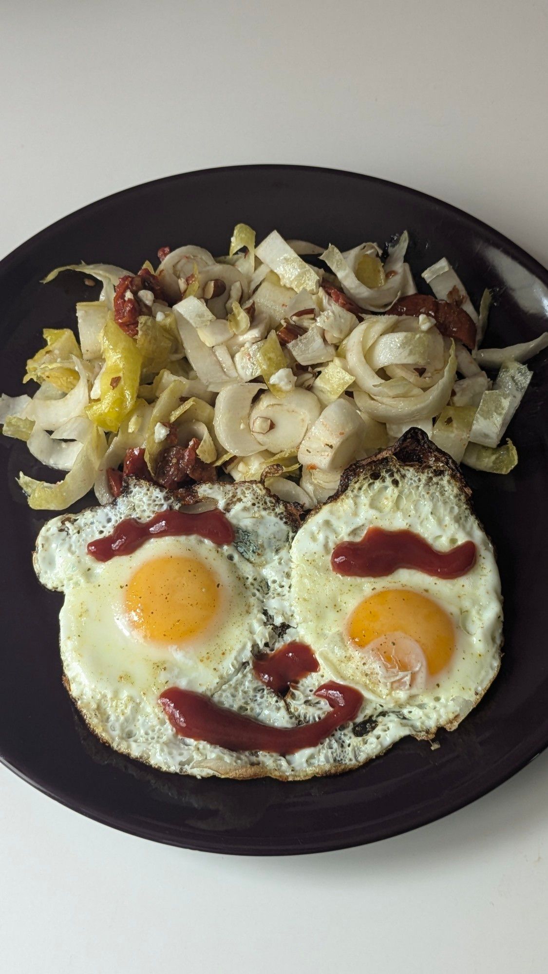 2 œufs au plat avec du ketchup qui dessine des sourcils, un nez et une bouche.  Salade d'endives au-dessus qui font les cheveux.