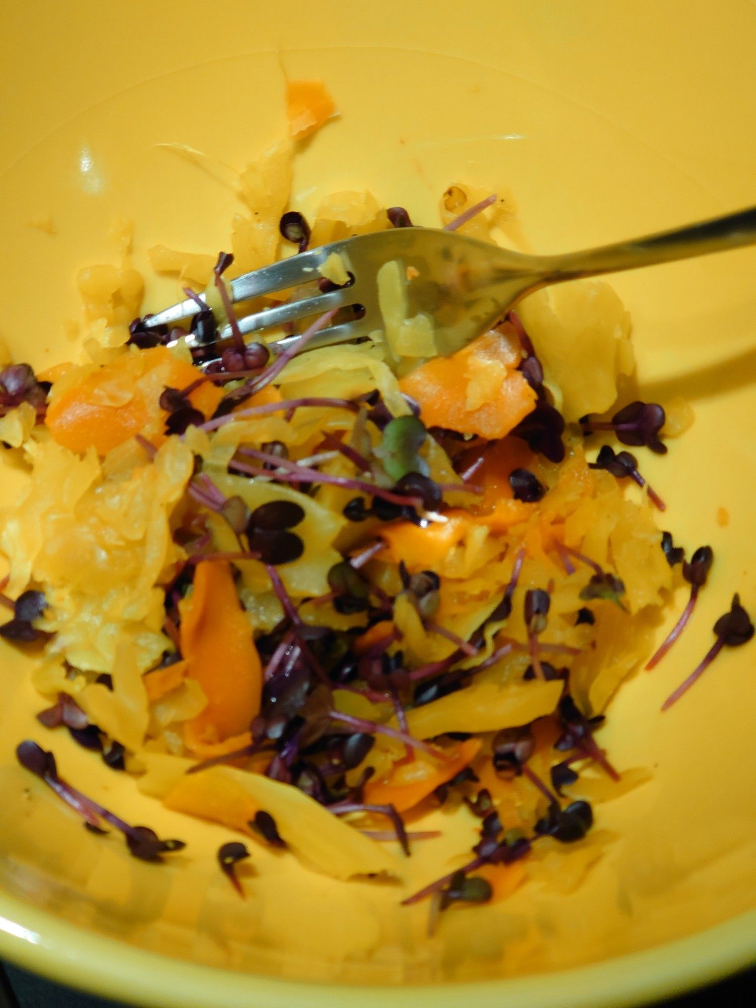 Salad with carrots and yellow cabbage in a yellow bowl, a fork stirring