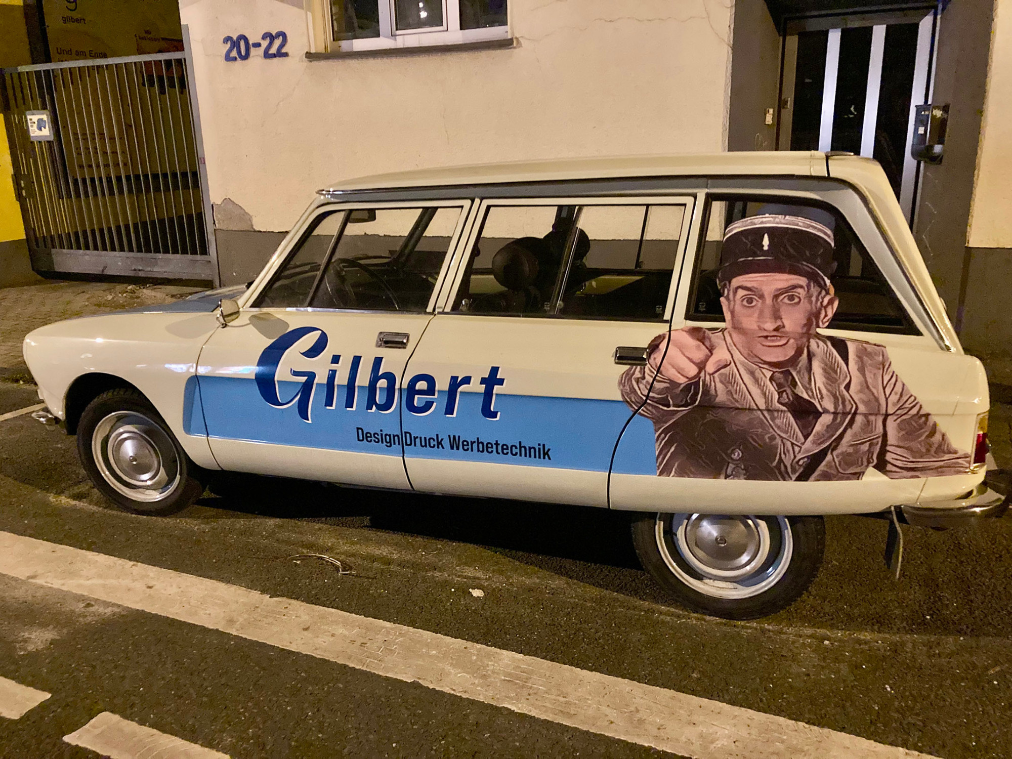 Photo d'une Citroën Ami 8 garée à Essen en Allemagne. Elle est décorée d'une photo géante du gendarme de Saint-Tropez (Louis de Funès). Il s'agit d'une publicité pour un fabricant de publicités adhésives.