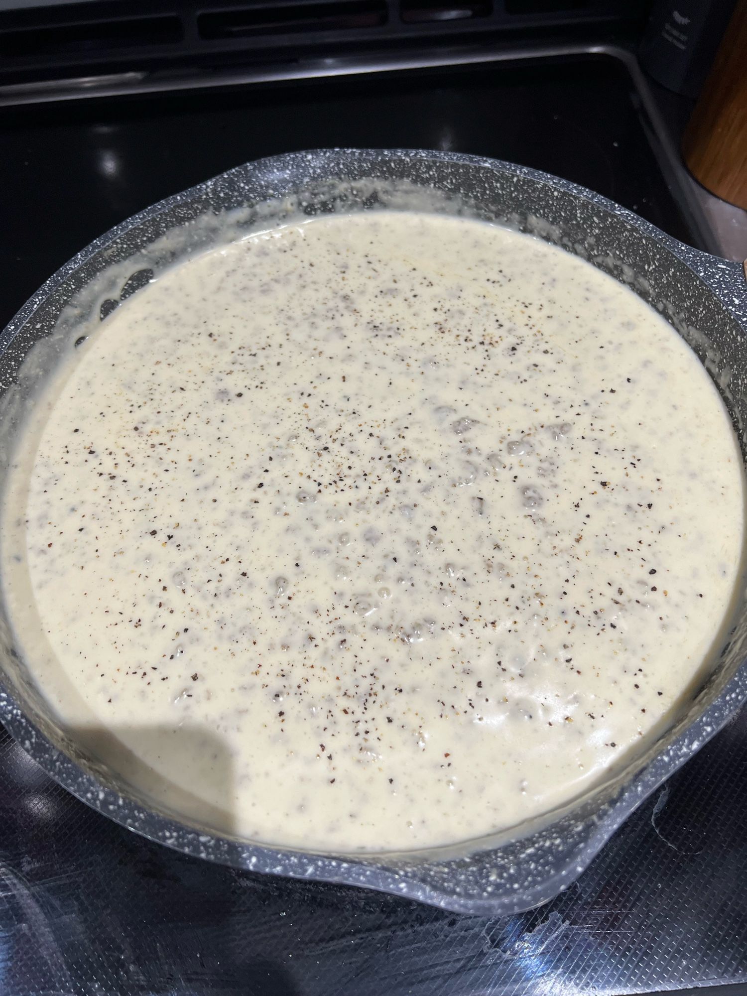 Decadent sausage gravy in a deep frying pan on a glass top stove