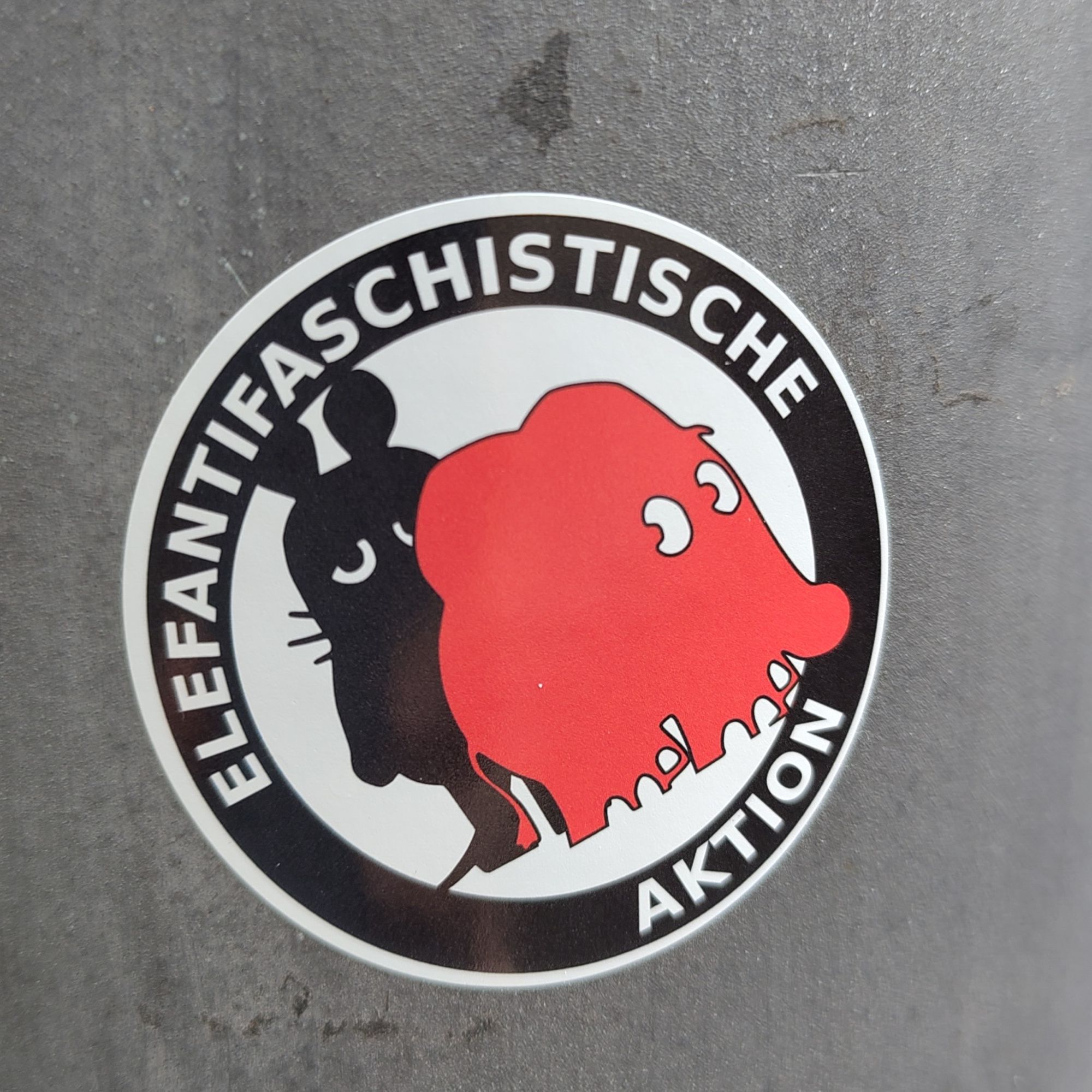 Ein Antifa Aufkleber auf dem Maus und Elefant im Stil der Figuren aus der Sendung mit der Maus abgebildet sind und auf dem steht "Elefantifaschistische Aktion". Der Aufkleber klebt an einer Laterne.