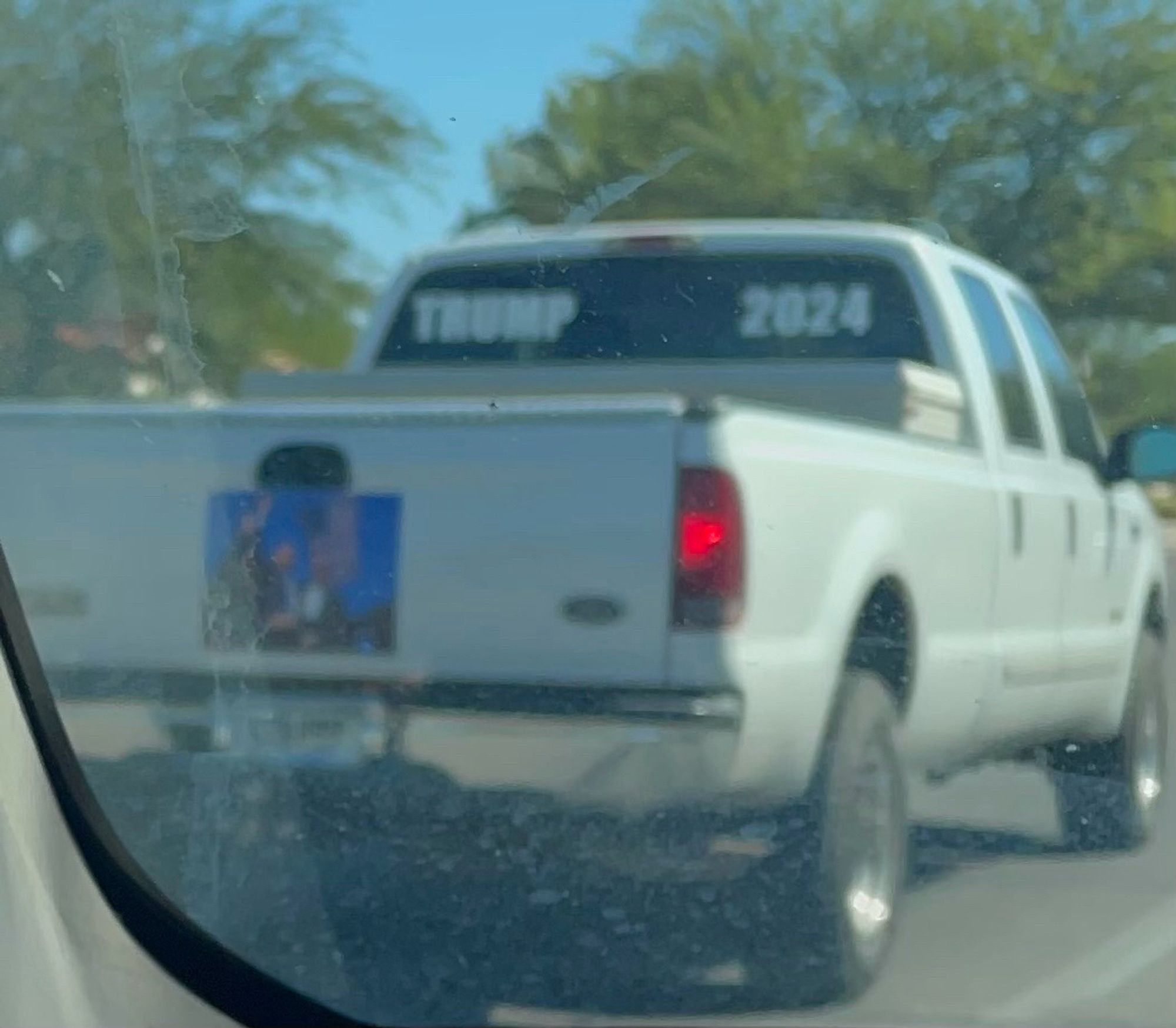 White pick up truck with TRUMP 2024 in large print in the back, and a huge picture of Trump doing the Jersey fist pump after the first assassination attempt.