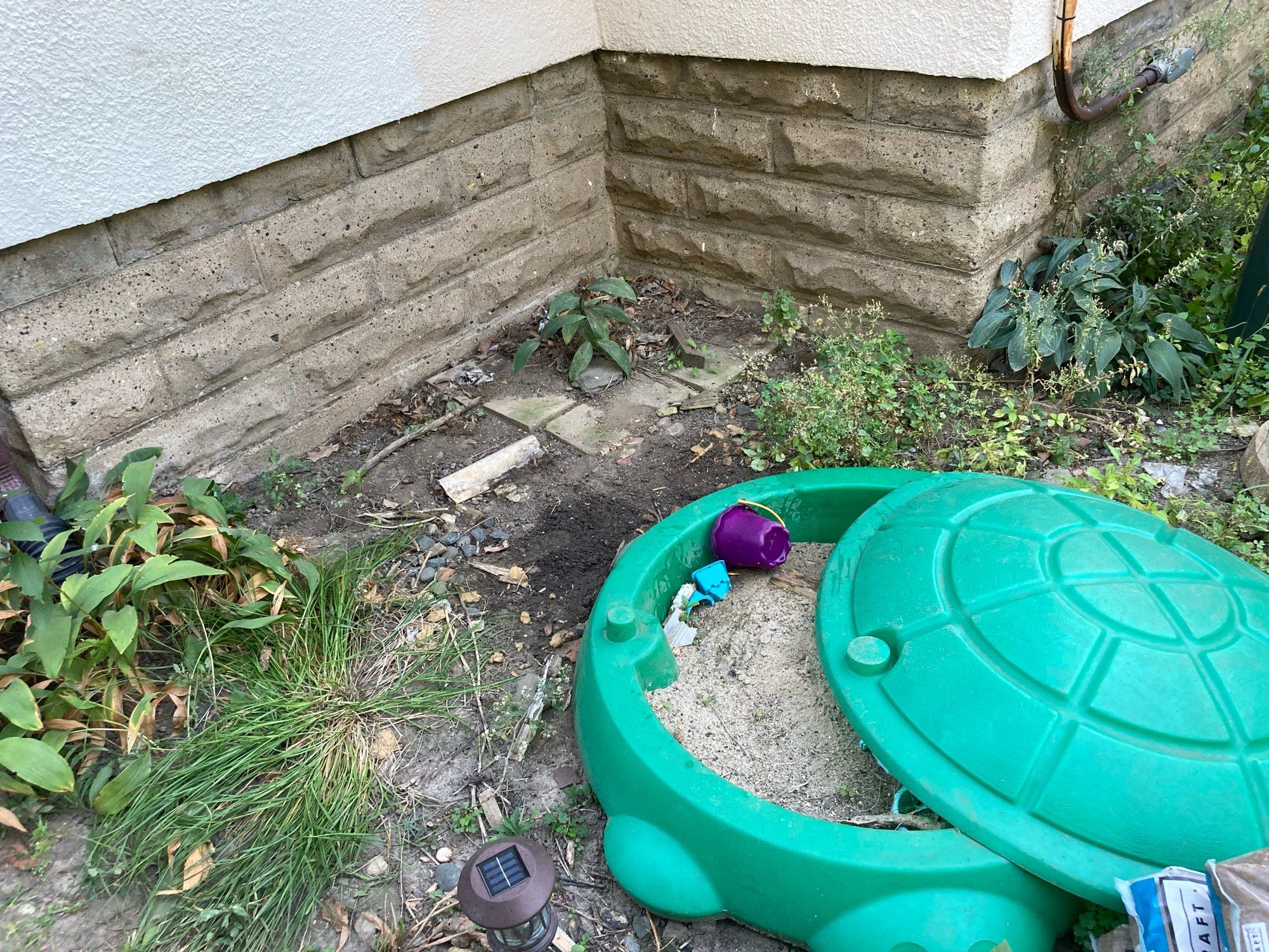 A corner of dirt and debris next to a house. There is turtle sandbox.