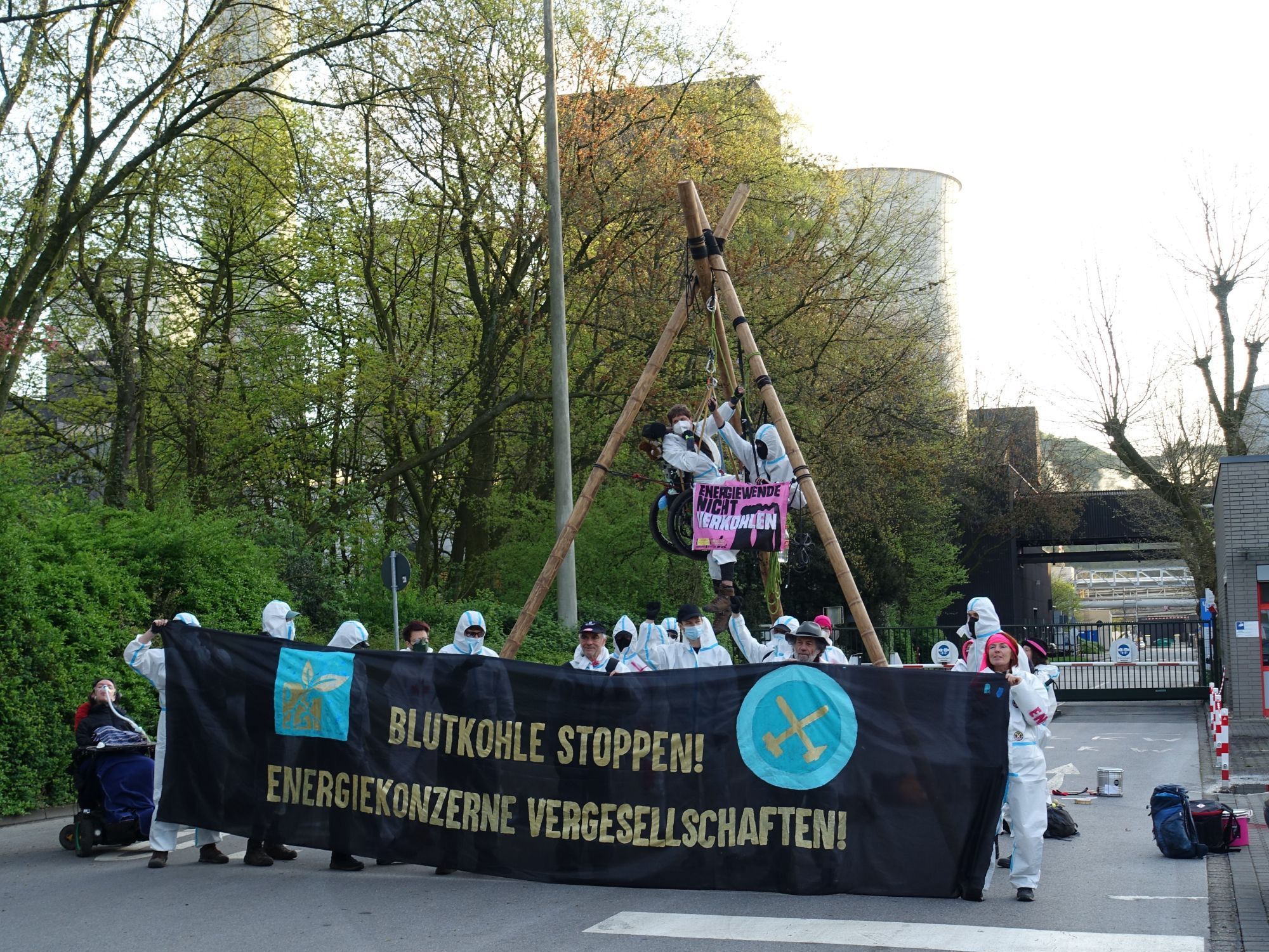 Aktion mit Tripod, 2 Menschen darin 8 1 davon im Rollstuhl), Menschen mit weißen Maleranzügen und banner Blutkohle stoppen energiekonzerne vergesellschaften