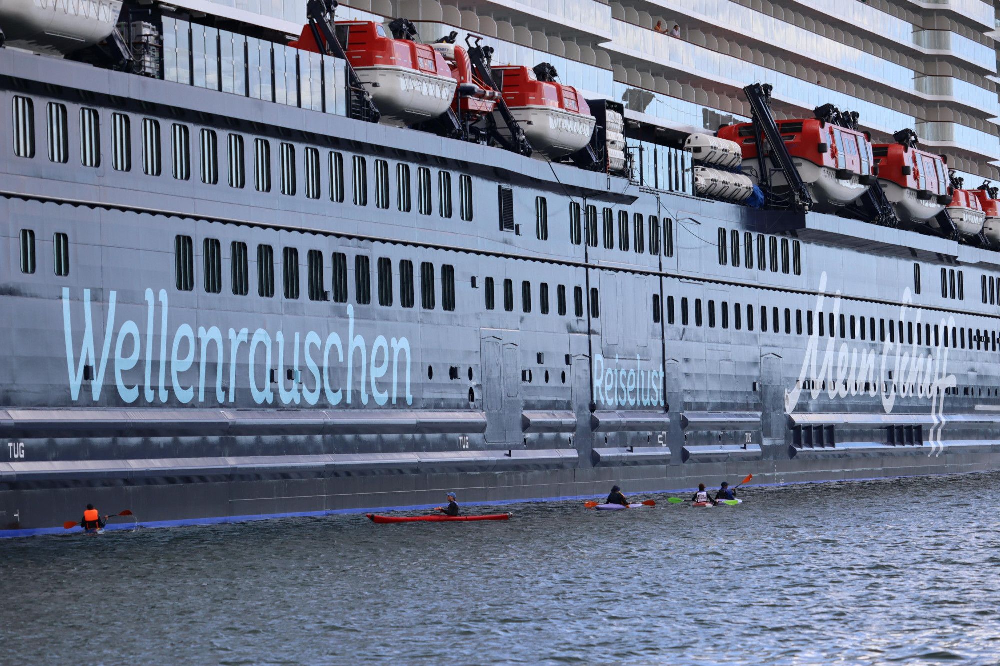 Menschen mit Kayaks, ganz klein auf Wasser neben der Wand vom riesigen Kreuzfahrtschiff