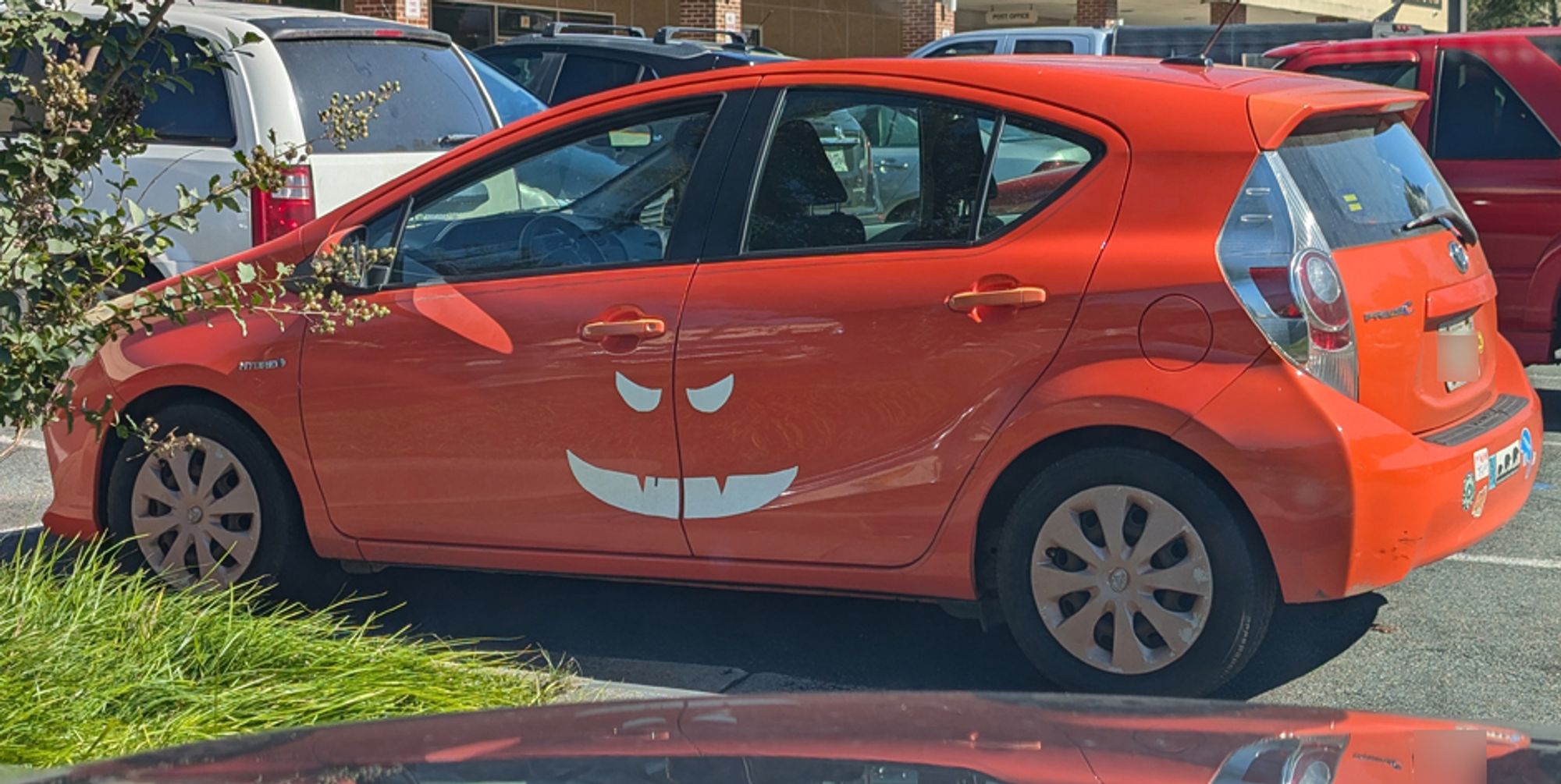 A cute orange Prius with a white decal on the door that makes it look like a jack-o-lantern.