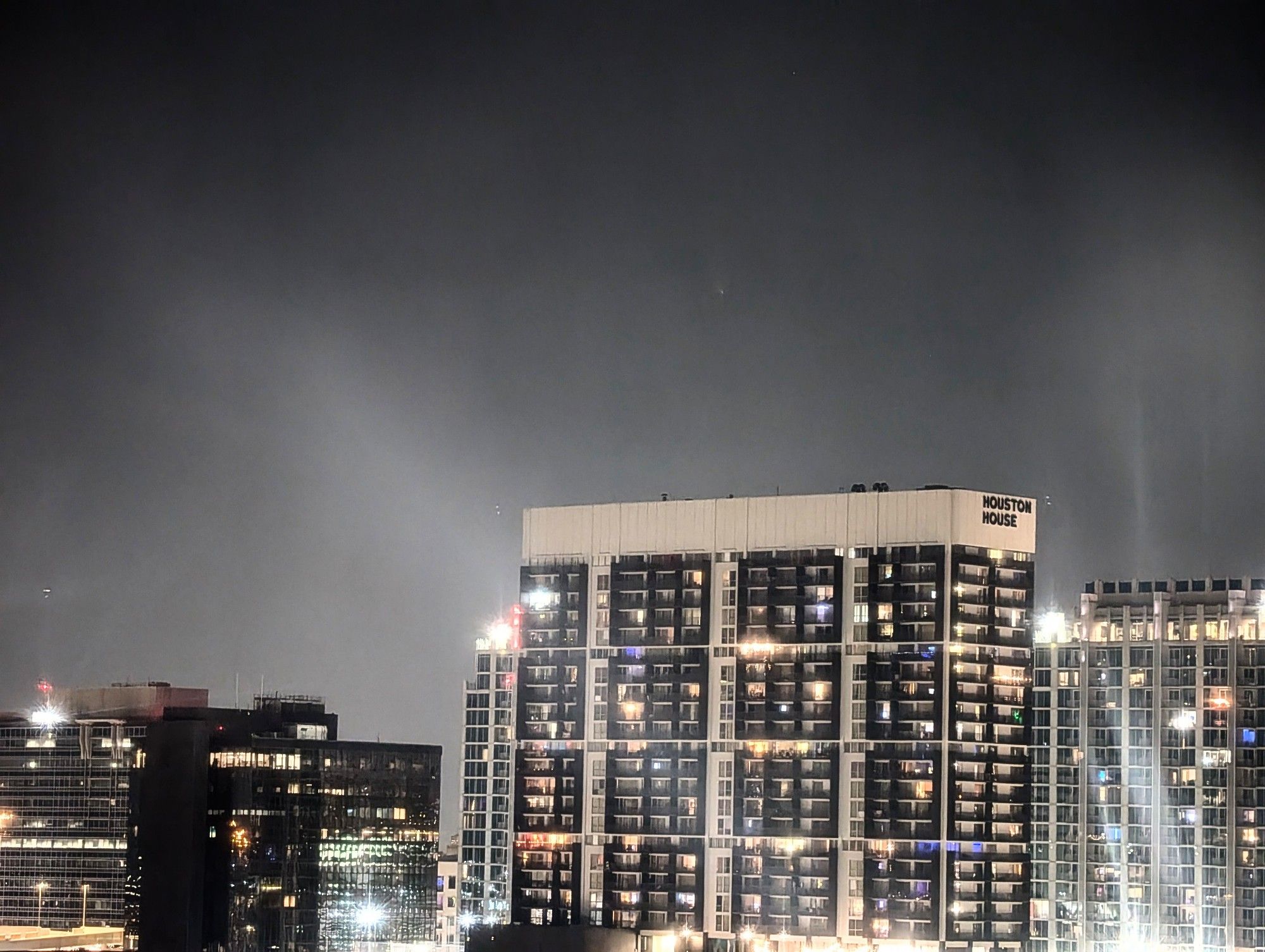 A building in Houston is at the bottom, and the comet is very faint as a fuzzy dot above it. 