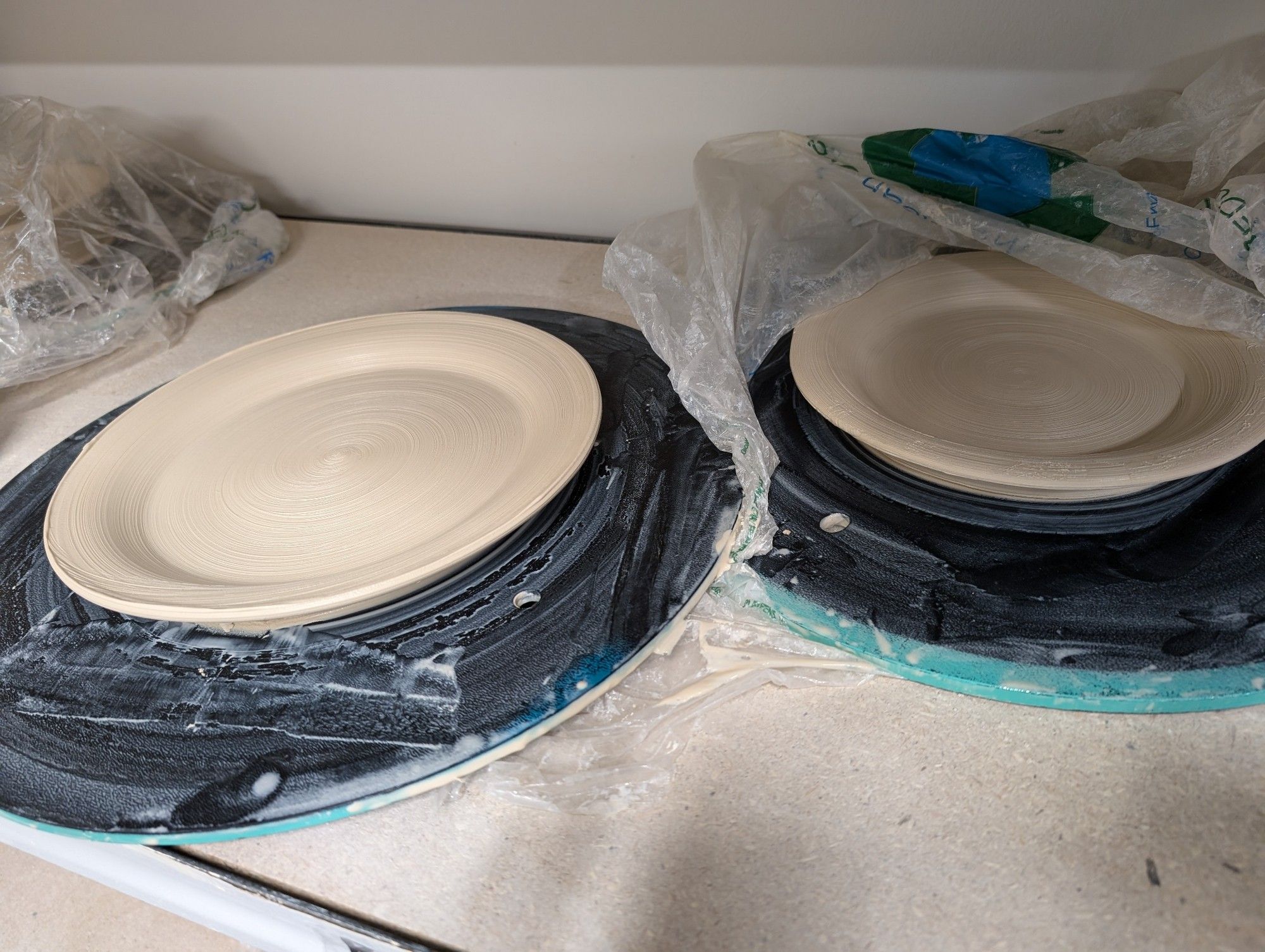 Two cream-colored clay plates drying on a shelf.