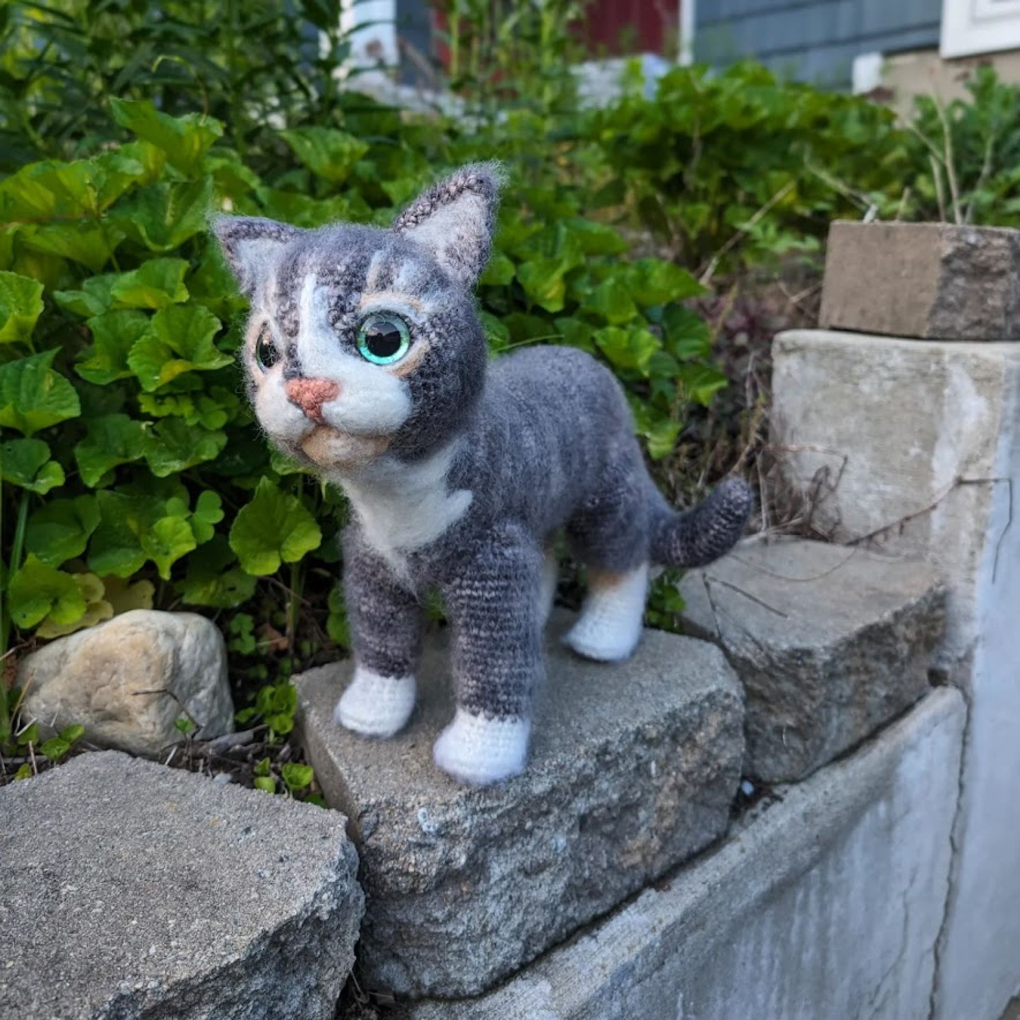 A gray tabby crochet cat posed on a garden wall.