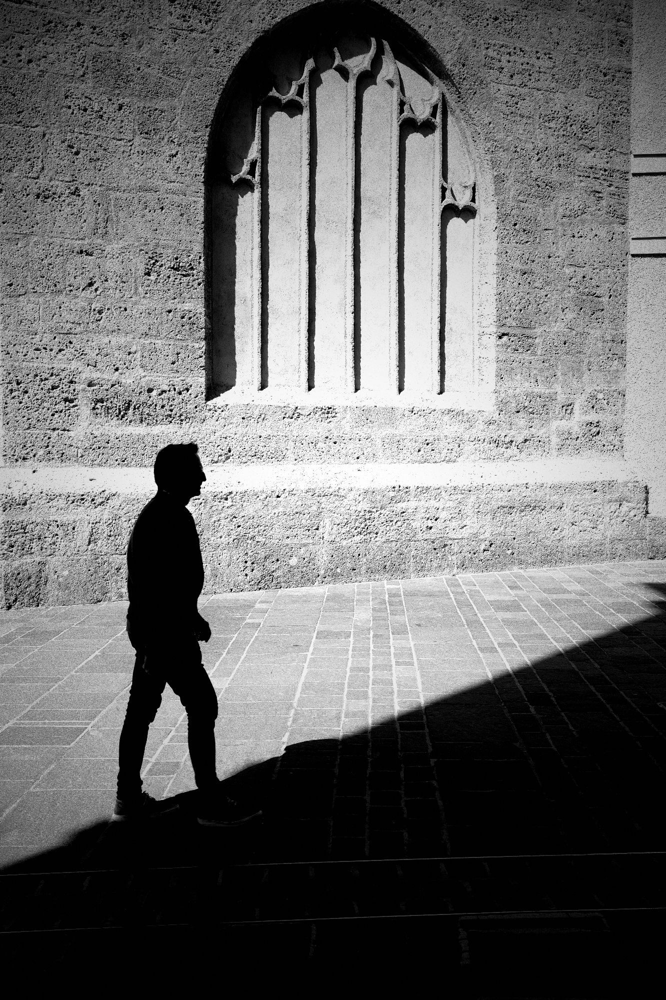 Fotografie in Schwarzweiß mit einer Ricoh GRIIIx. Im Hintergrund eine Kirchenmauer in starker Sonneneinstrahlung. Davor ein kräftiger fast schwarzer Schatten mit einer ebenso dunklen Person.