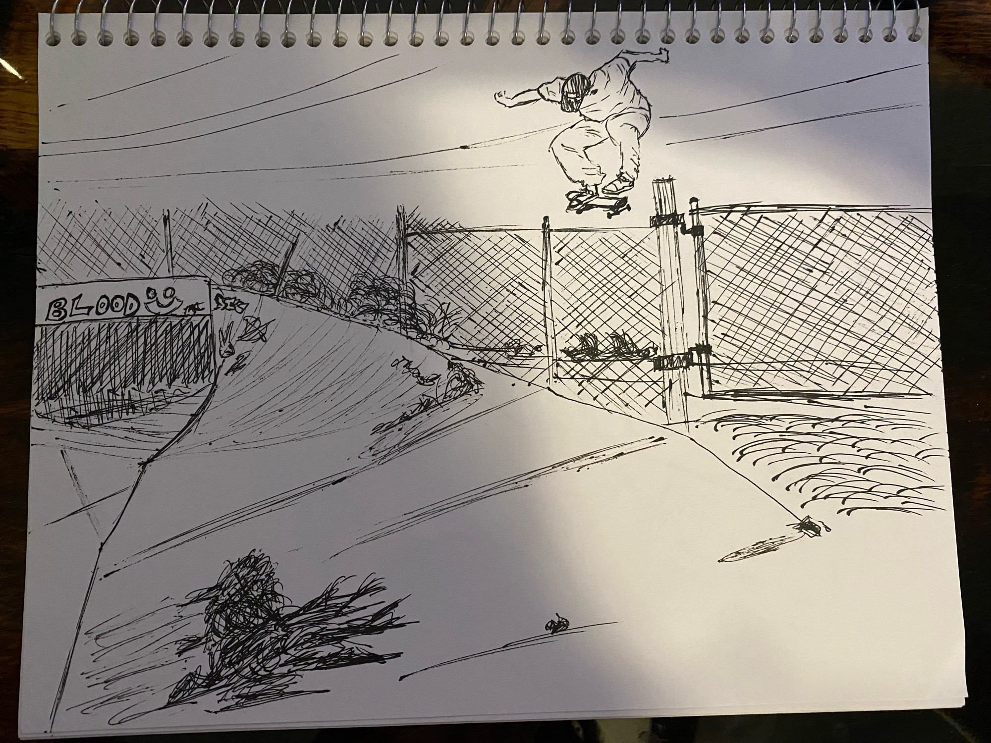 a drawing i did in thin sharpie in a sketchbook of a skateboarder doing a jump in an empty lot surrounded by a chain fence