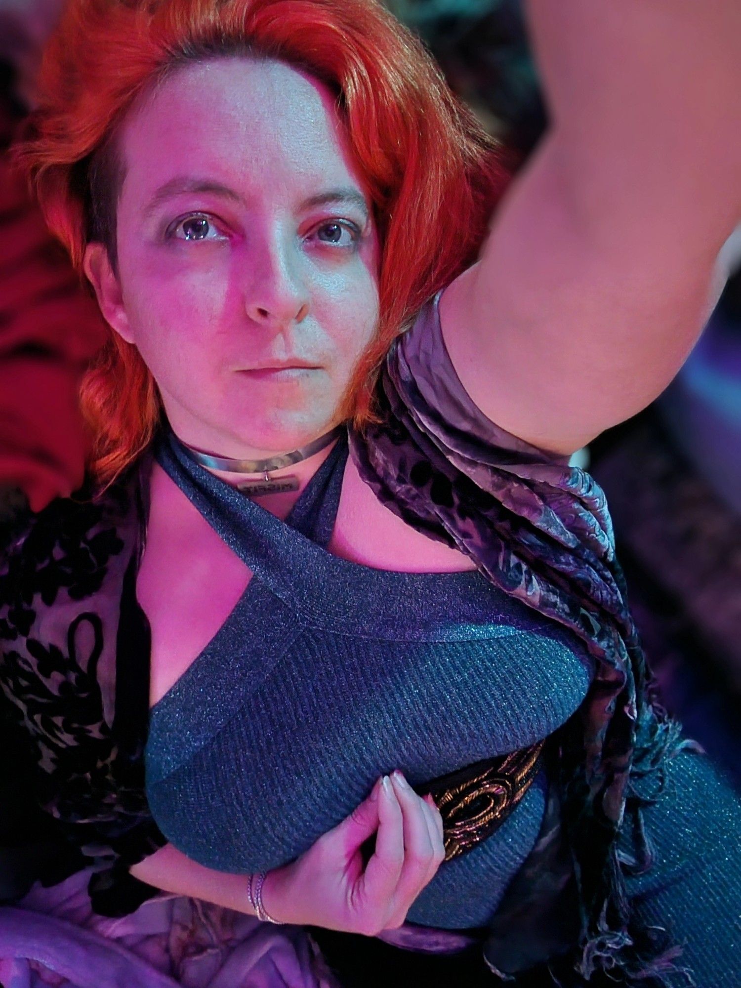 Myself, long red hair with a side cut, tight, sparkly emerald dress, purple floral scarf taking a selfie.