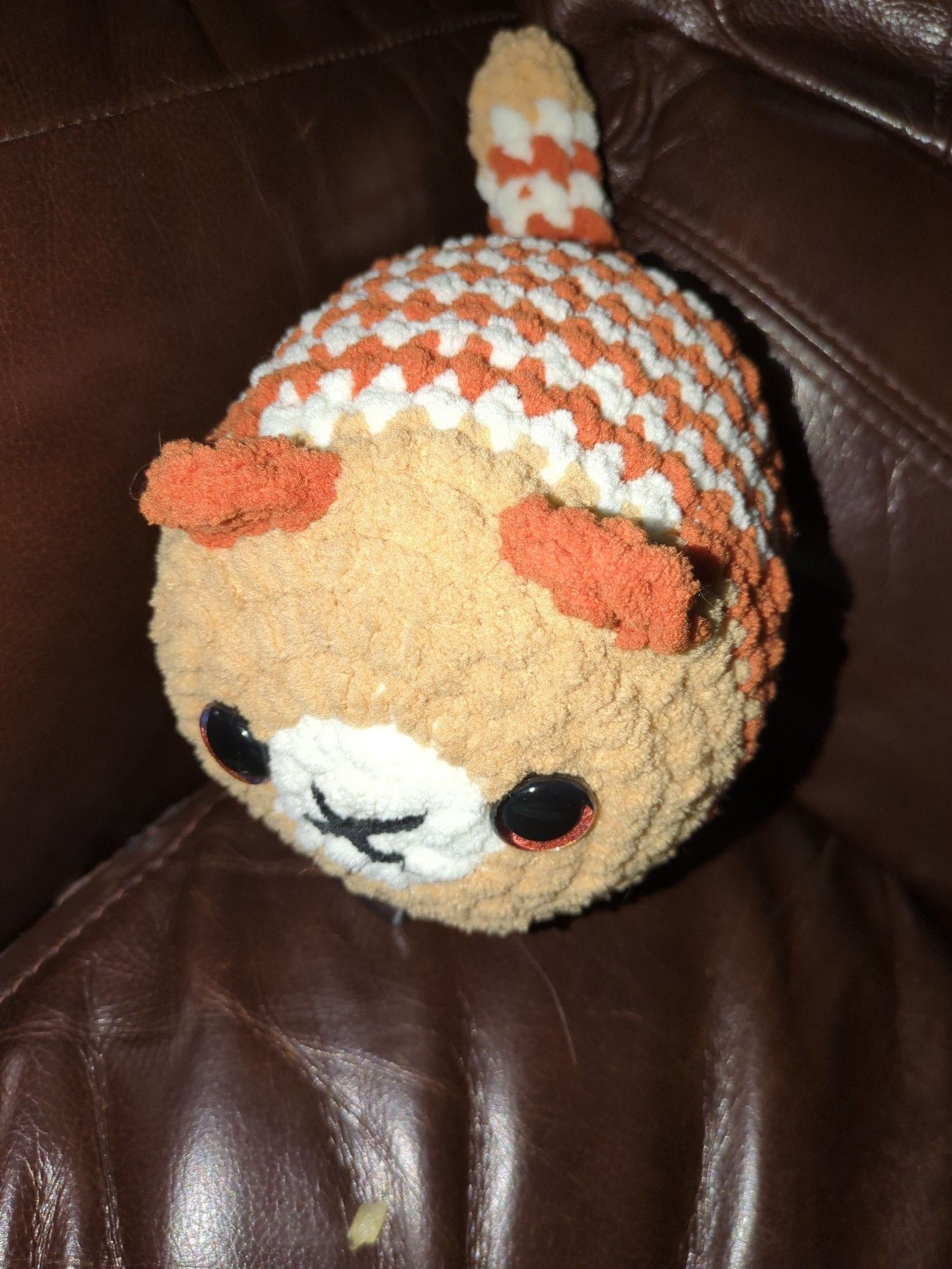 A handmade crocheted cat in plush yarn in shades of orange, cream and caramel.