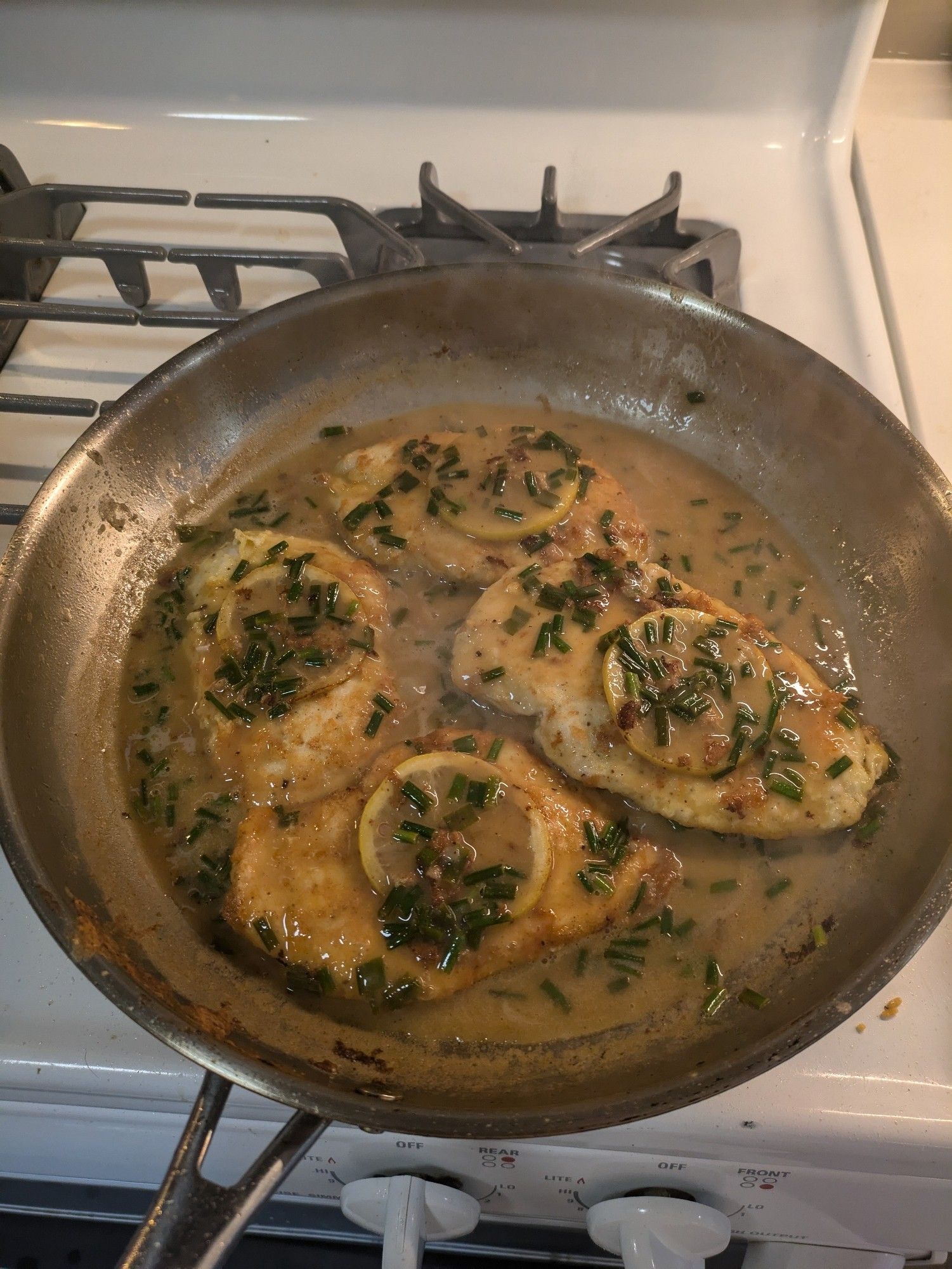 Golden chicken breasts with little slices of lemon on top, all resting in a yellow-brown sauce in a skillet