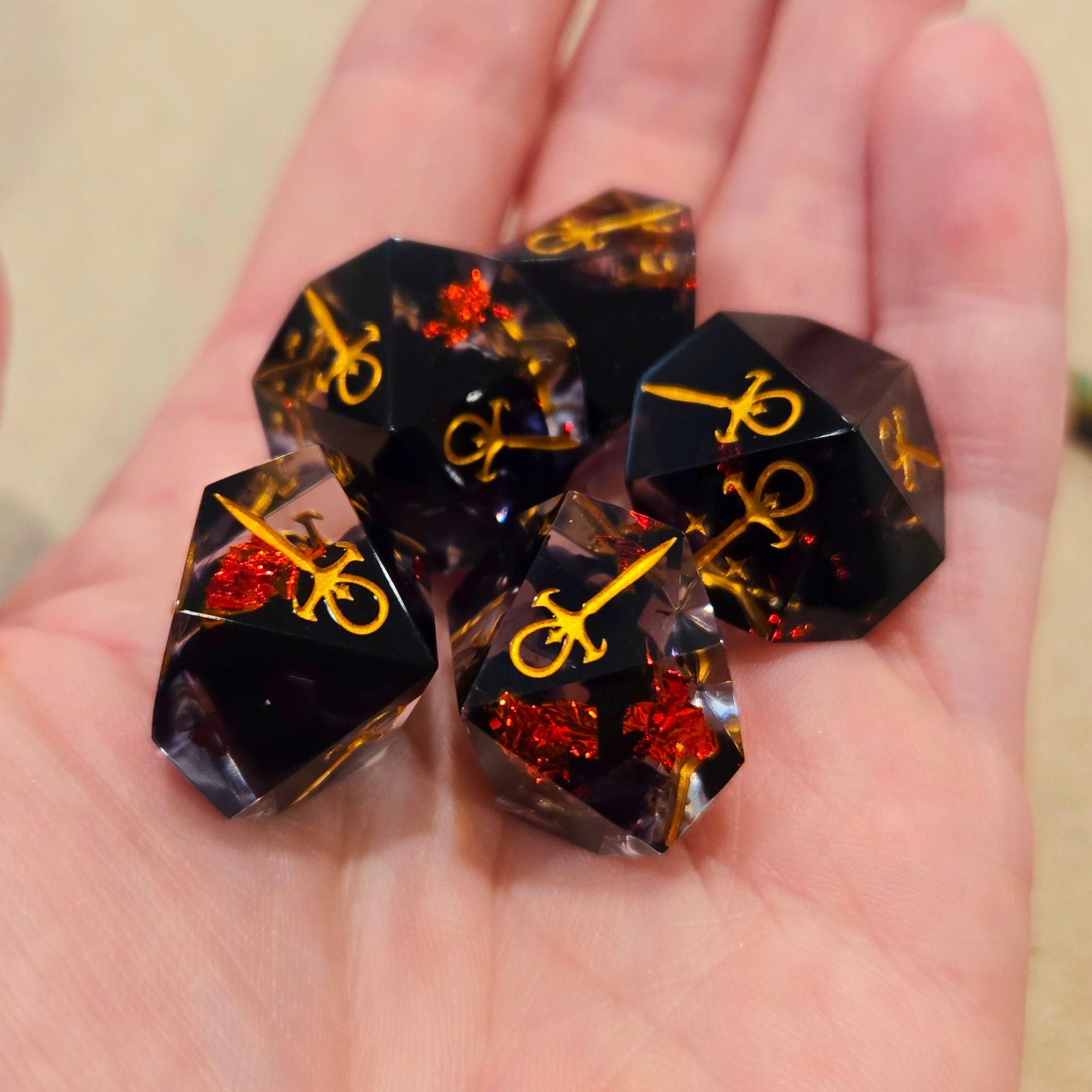 5 Vampire the Masquerade hunger d10s in an open palm. The dice are clear with red foil and black ink swirled throughout. The engravings are inked in gold. 