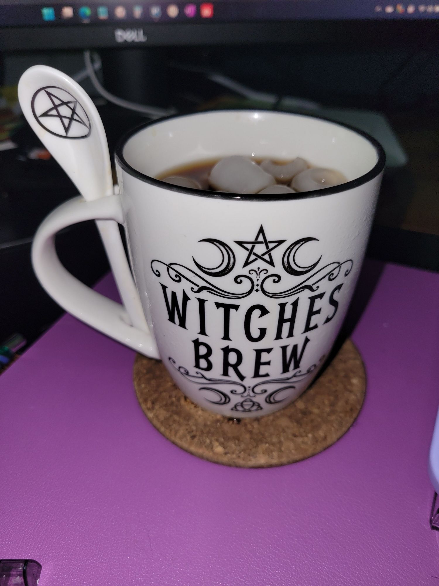 Coffee mug filled with iced coffee. Text reads Witches Brew. Spoon attached with handle with pentagram symbol in spoon itself.