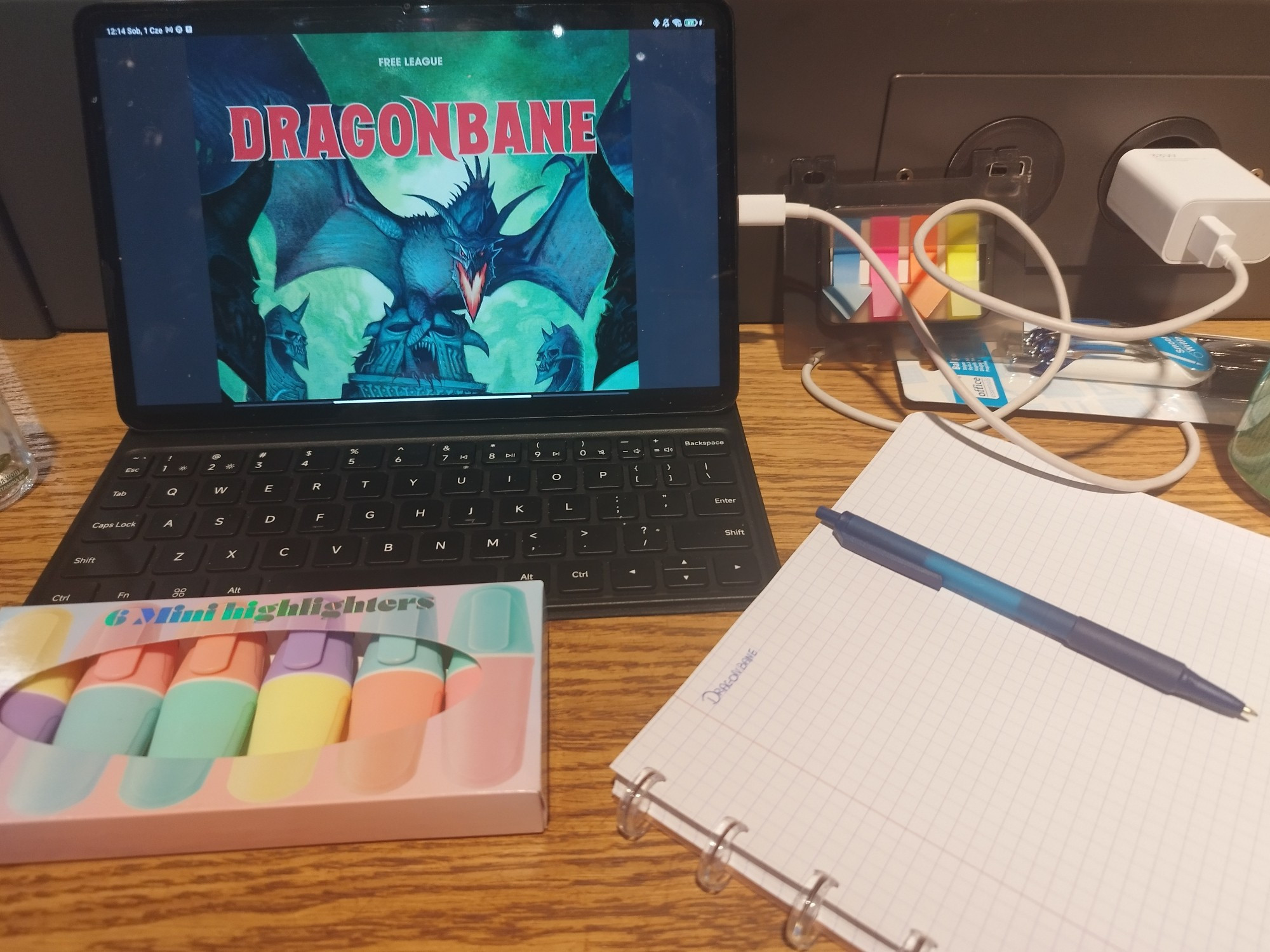 A set up at a table in a cafe. Tablet with open Dragonbane Corebook, highlighters, notebook and some sticky notes.