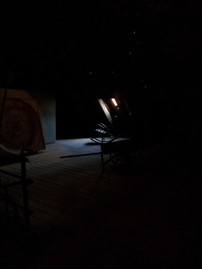 A dark room. Light through a small window shows an old rocking chair.