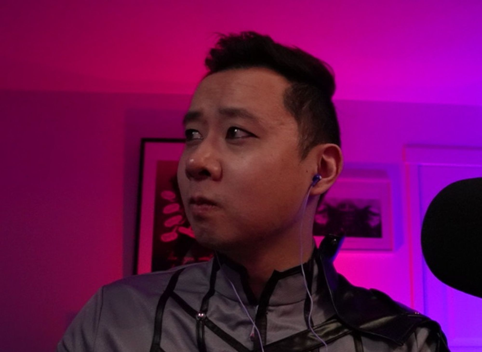 Matt is wearing a black and grey patterned zip-up shirt, a black leather shoulder pauldron, looking off into the distance with purple and red in the background