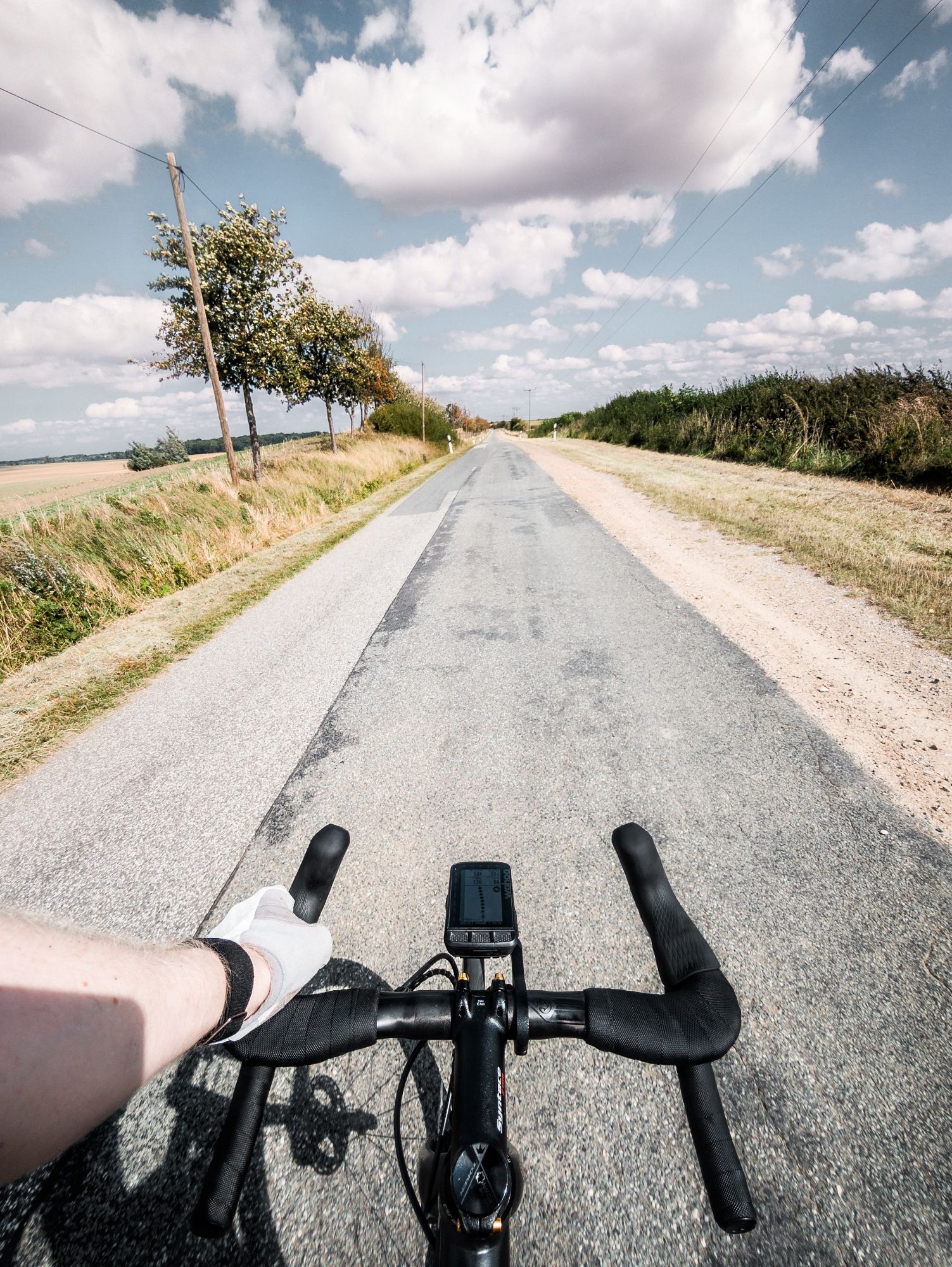 eine geflickte strasse mit teilweise bewölktem himmel, im Vordergrund ein Rennradlenker