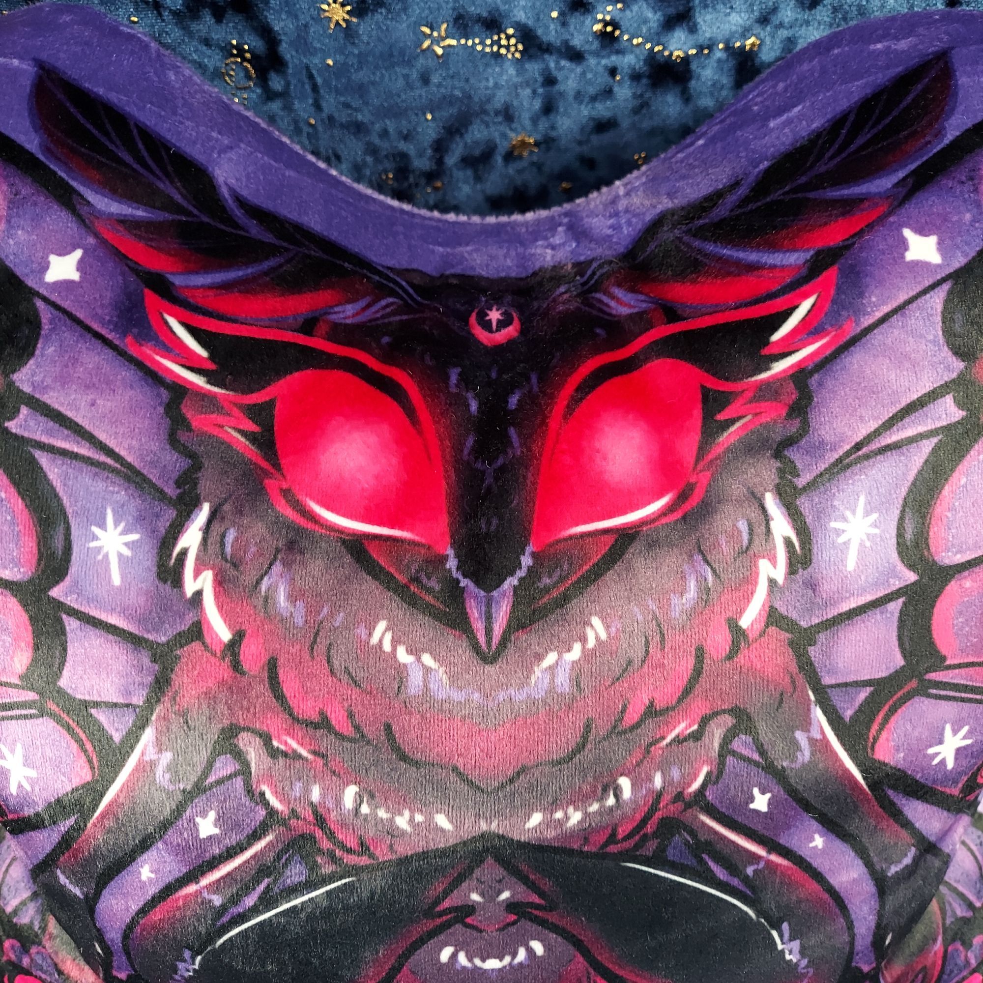 A close up of the face of the Mothman fairy plush, to show off how well the drawn details printed -even the small detials such as the subtle gradient on the moon and star foreheeard marking, and the tiny stars and moth fluff highlights. The close up also shows off the fuzzy velveteen texture his is printed on.