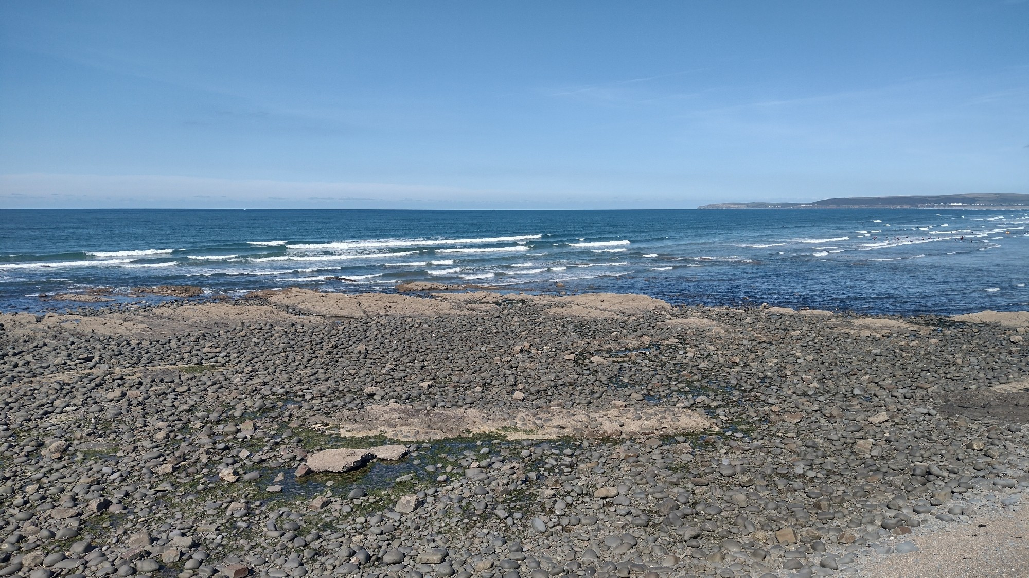 Image of a wide expanse of sea with rocks and cobbles in the foreground.