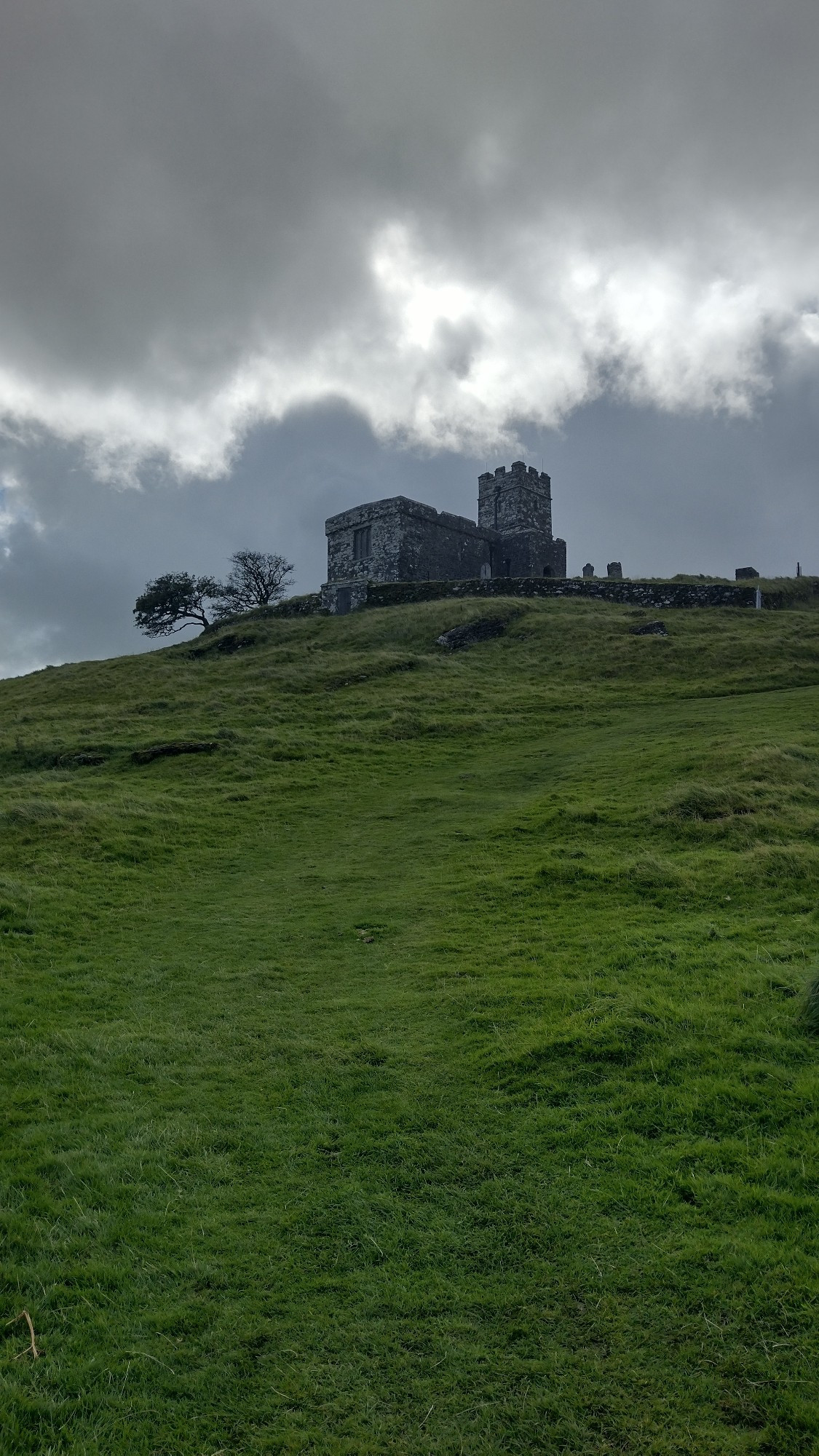 Upward view at a church sat at the summit of a hill.  There is a raincloud above.