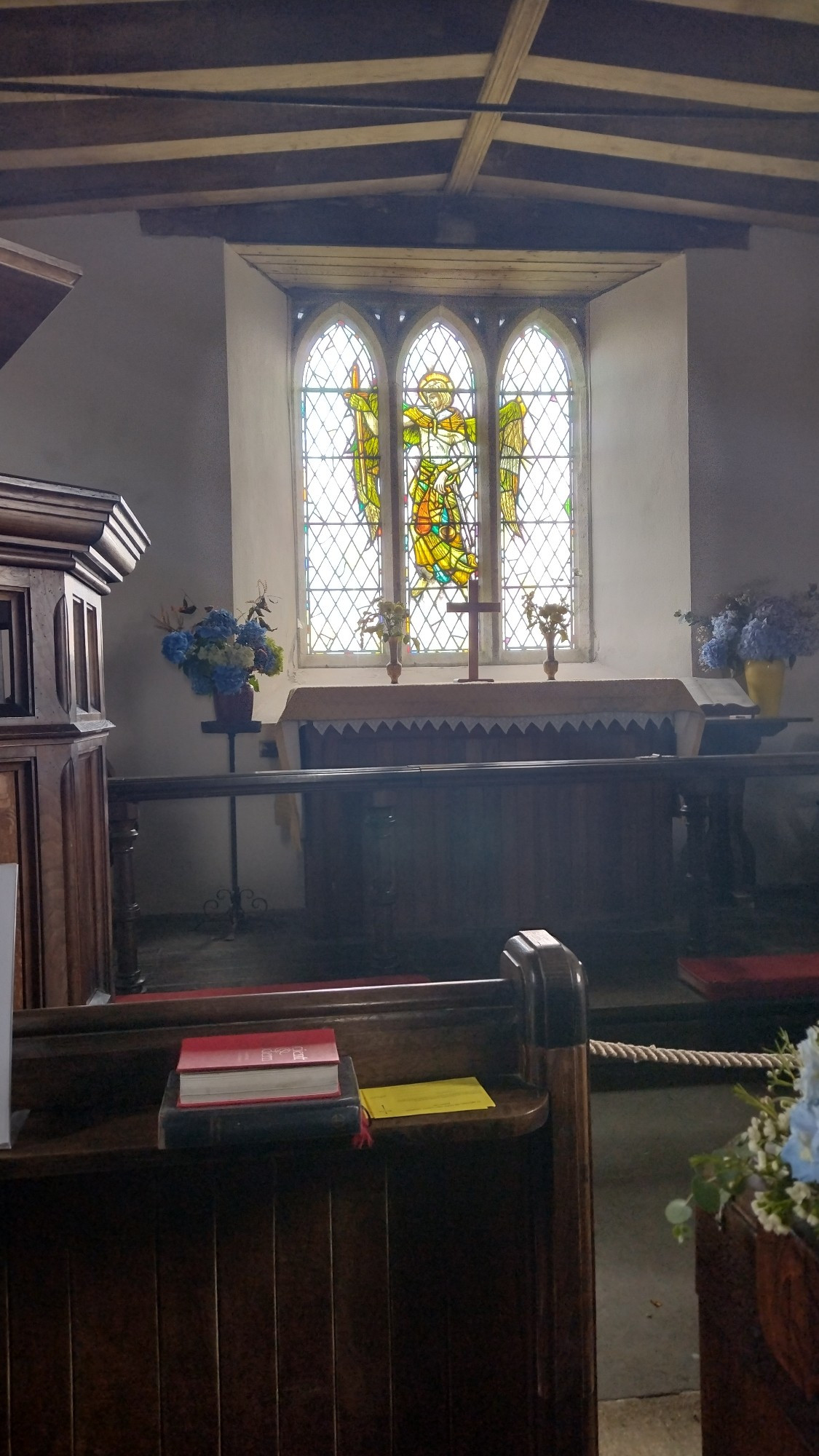 Inside of a small church with stained glass window of St Michael at the back.