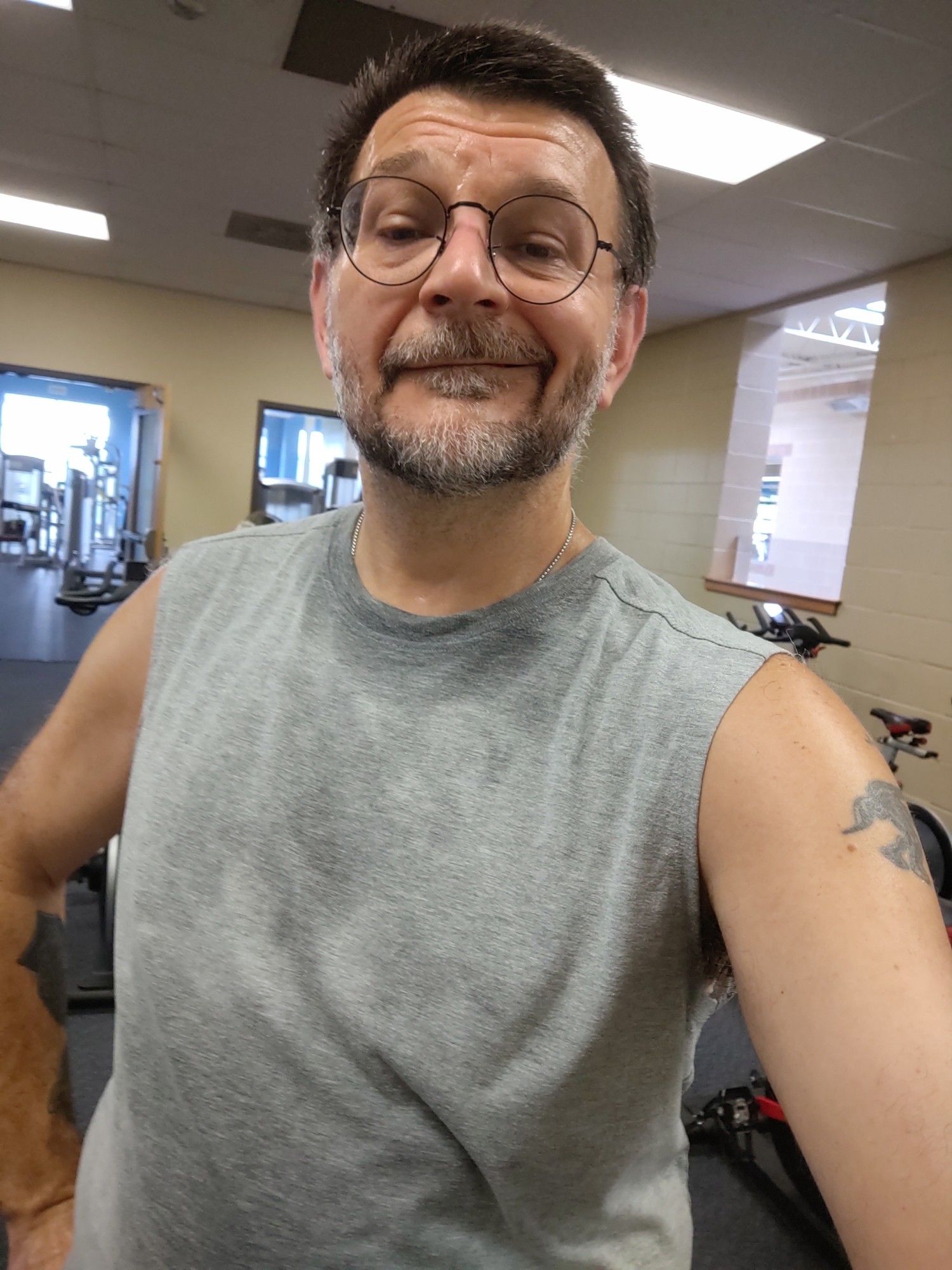 Sweaty me in a gray muscle shirt. I have a tired lopsided smile. You can just make out some exercise bikes behind me.