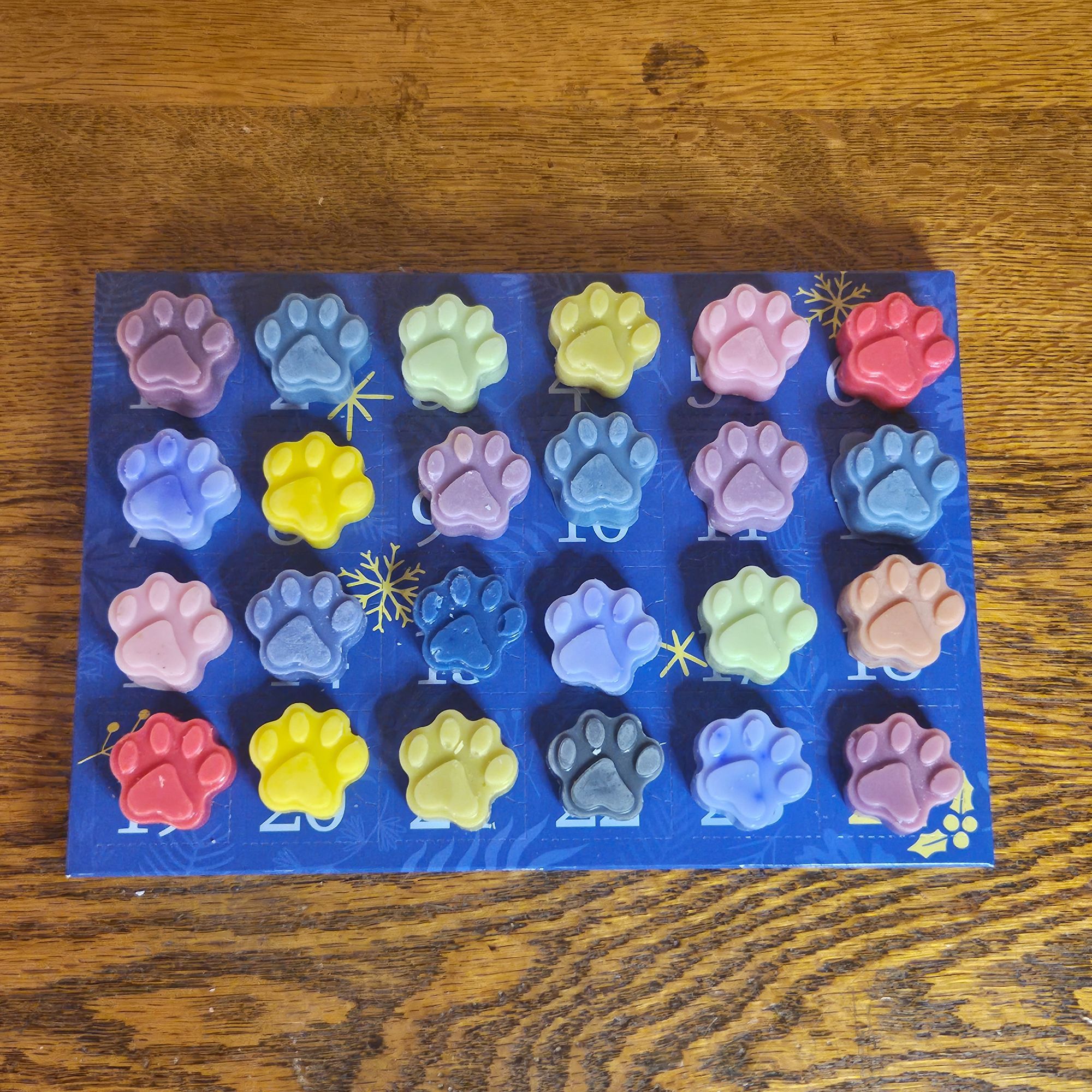 24 paw shaped wax melts on top of an advent calendar box on a wooden surface.