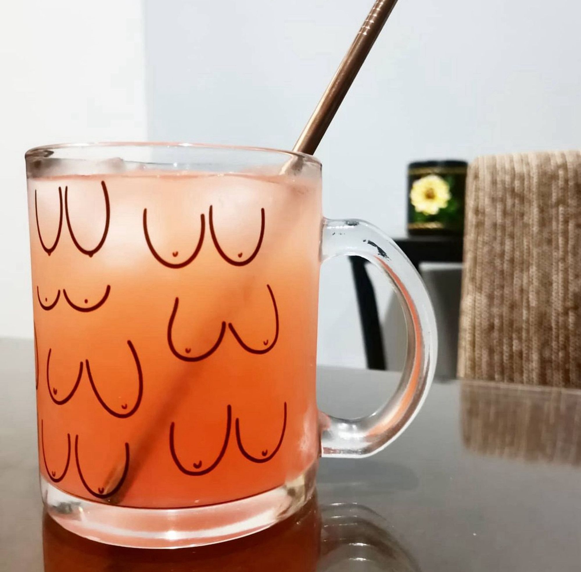 Glass cup with different shapes and sizes of breasts as a design. A copper straw sticking out of it.