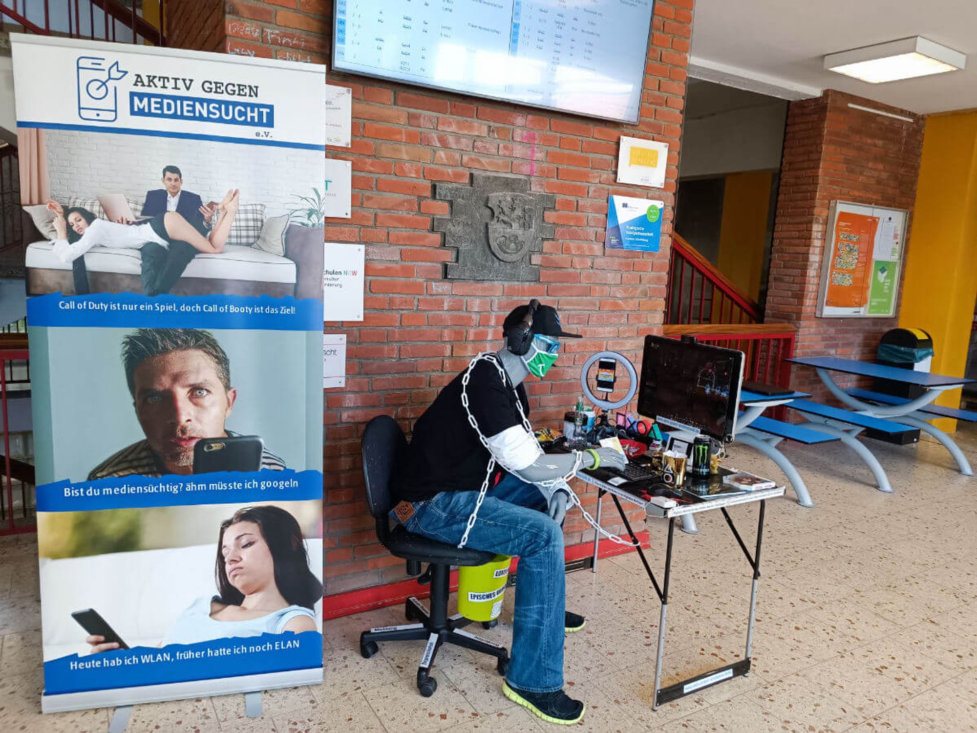 Bild von der Installation Felix einer Initiative gegen Mediensucht.
Neben der Figur ist ein Plakataufsteller, auf dem ganz oben ein Bild von einem Mann ist, der auf einer Couch sitzt. über seinem Schoss liegt eine Frau mit sehr knapper unterhose und pullover bekleidet. Die Bildunterschrift lautet "Call of Duty ist das Spiel, Call of Booty ist das Ziel"