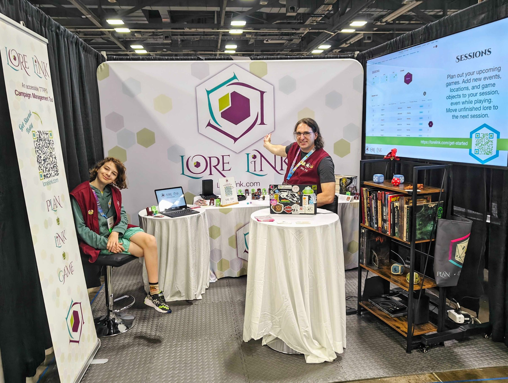 Photo of the Lore Link booth at Origins, with tables for demos, banners with the logo, and Lore Link team members ready to talk to guests.