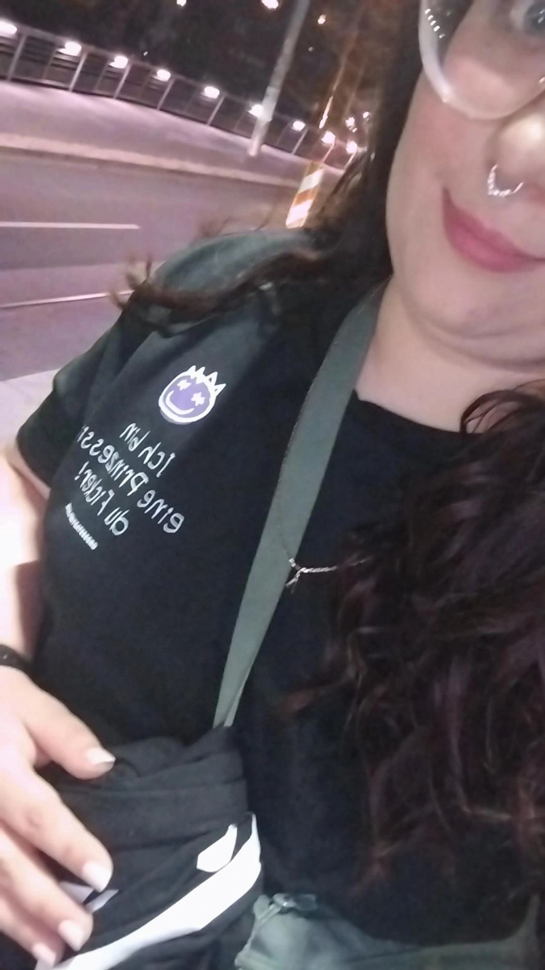 Mein halbes Gesicht mit Brille und Septum Piercing. Eine grüne anmutende Tasche um meine Schulter. Ich trage ein schwarzes Shirt von Grossstadtgeflüster mit dem Spruch "Ich bin eine Prinzessin du Ficker!"