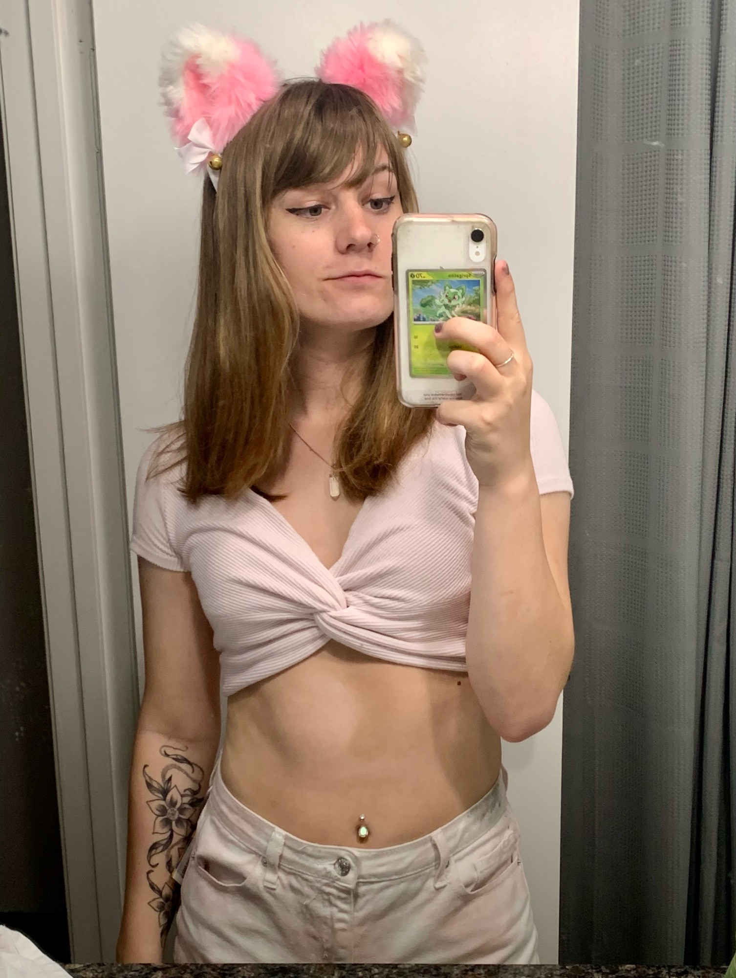 selfie of me w pink ears, a small pink top, my belly button pierced, and a flowery tattoo on my right arm 