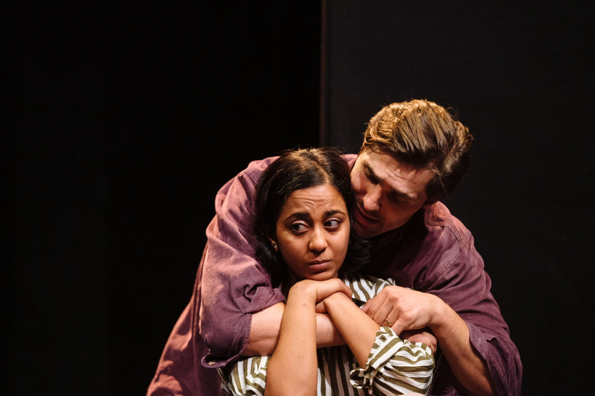 Anjana Vasan as Sylvia looks to the side with a worried expression, while Phil Dunster as Ray hugs her and tries to comfort her. BRACE BRACE at the Royal Court's Jerwood Theatre Upstairs, 2024.