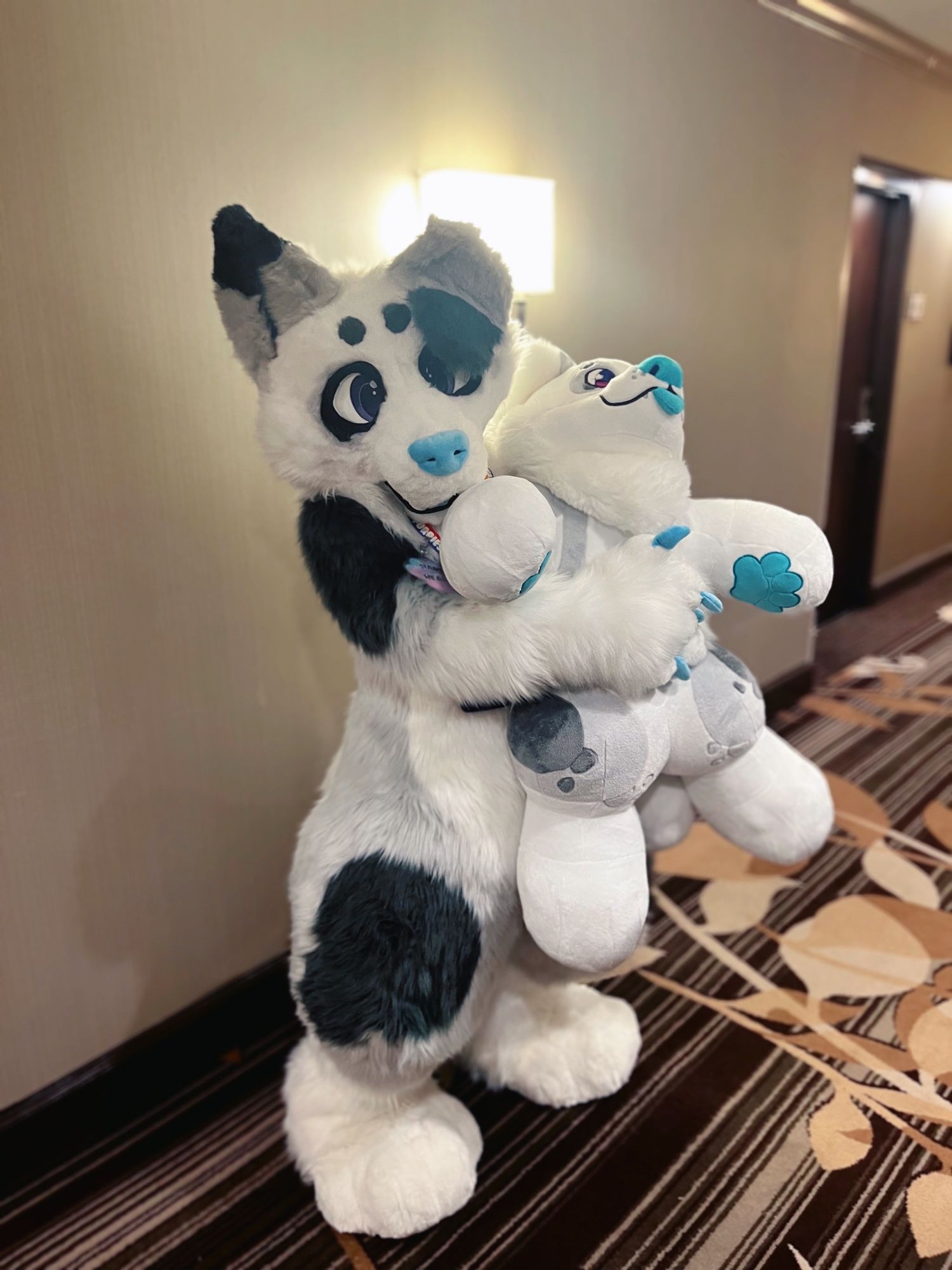 A white and gray dog fursuiter holding a huge plushie of themself.