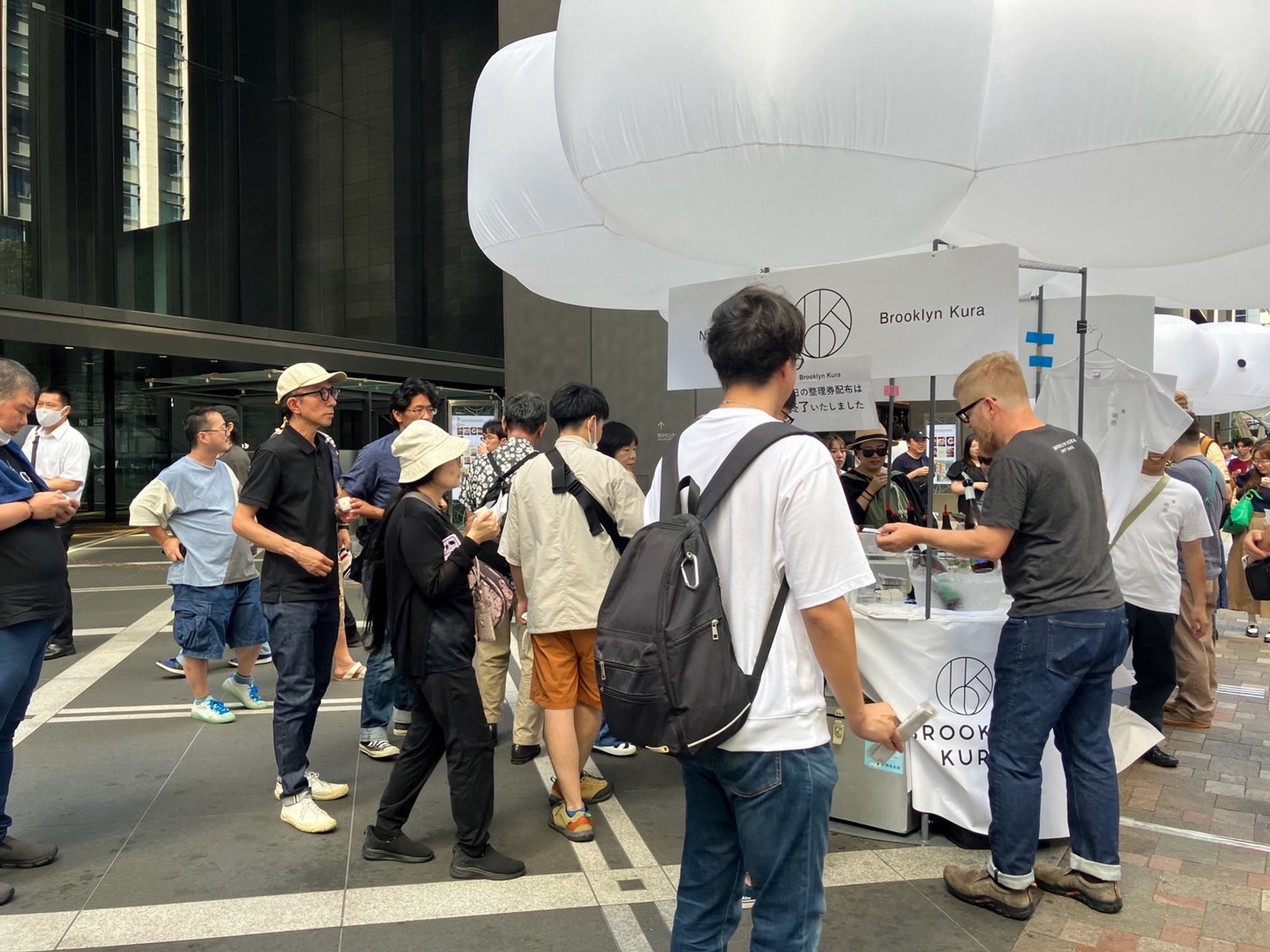 Me serving sake to folks at an outdoor sake event. Our tables have cool/weird white balloons above them.