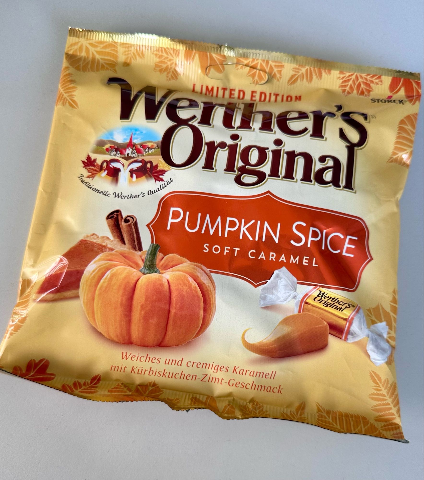 Eine Tüte Werther's Original Pumpkin Spice Soft Caramel. Auf der Verpackung sind Kürbisse, Zimtstangen, die Bonbons verpackt und unverpackt drauf. 
Insgesamt ist die Tüte sehr herbstlich gestaltet, mit Blättern am Rand in verschiedenen Orangetönen. Insgesamt ist die Tüte beige-gelb.