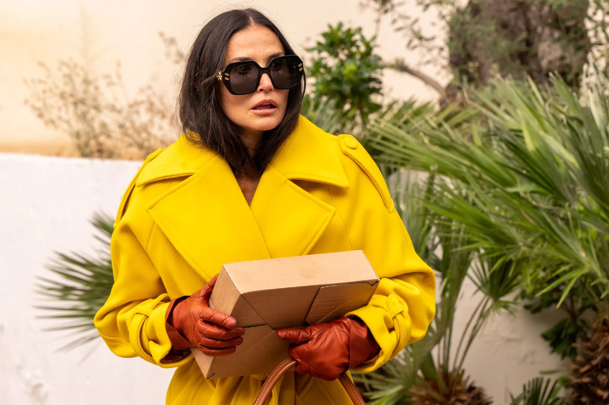 Demin dressed in a fab canary yellow trench coat in The Substance. 