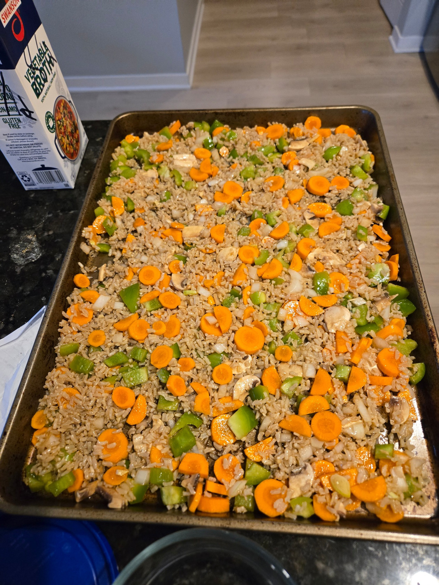 A baking sheet filled with rice, carrots, green bell pepper, onion, garlic, ginger, and some oil/vinegar. Not yet baked or with egg added