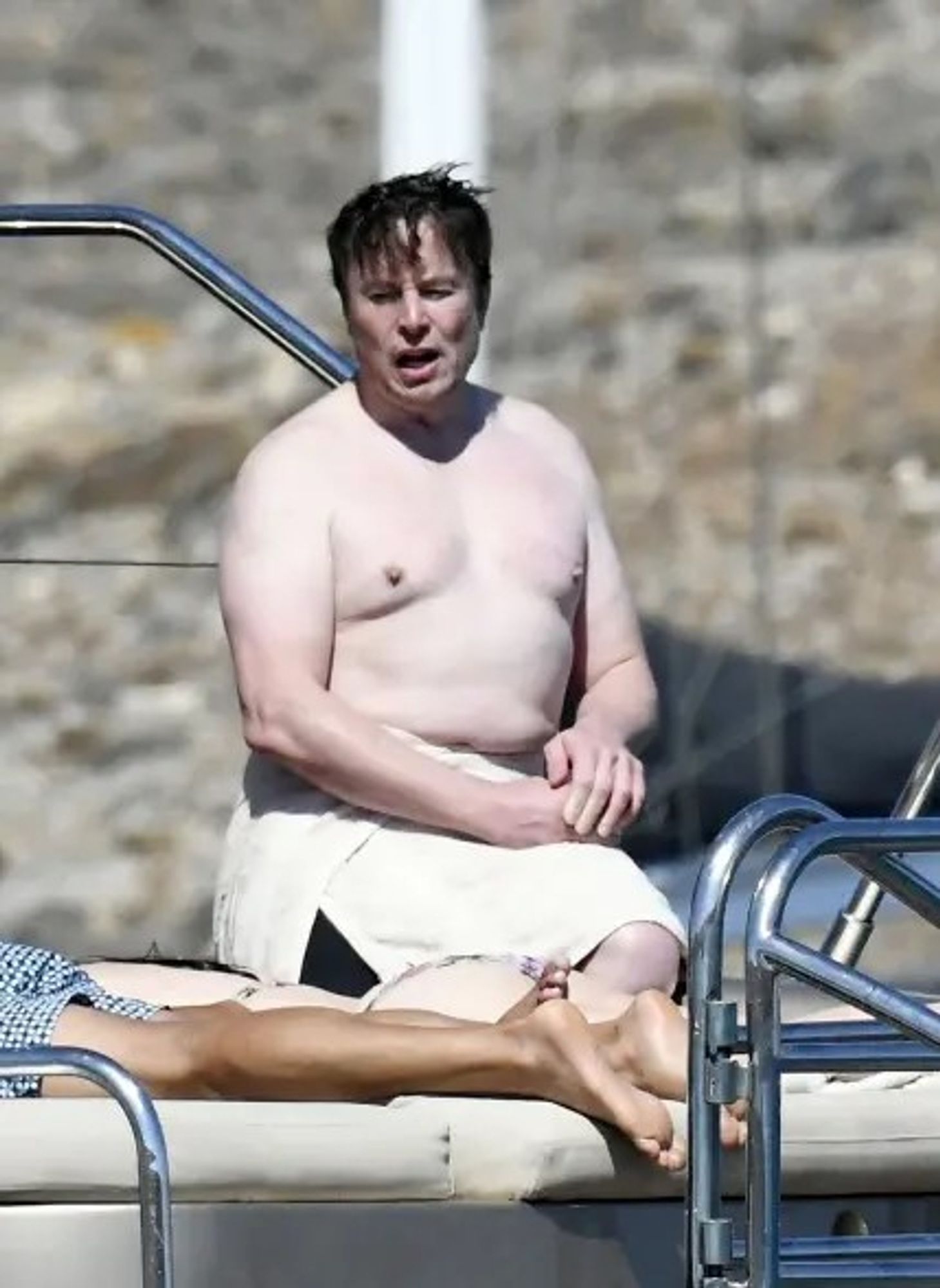 Fat Elon Musk. No body hair below his head. No muscle tone (he couldn't punch his way out of a paper bag). Musk sitting on a boat with no shirt.