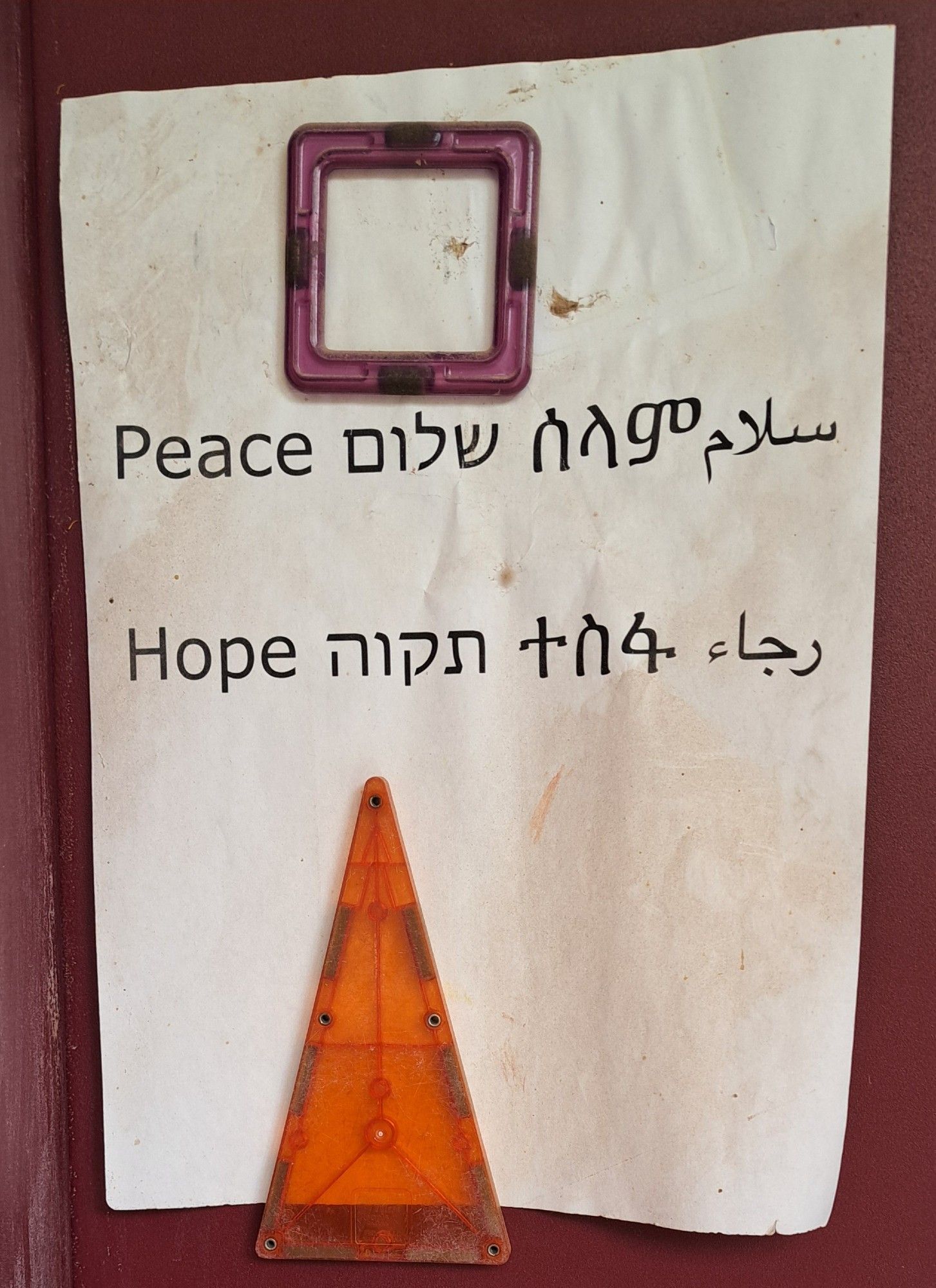 A paper sign pinned to a door with Magna Tiles. The sign says, "Peace, Hope" in English, Hebrew, Arabic and Tigrinya.