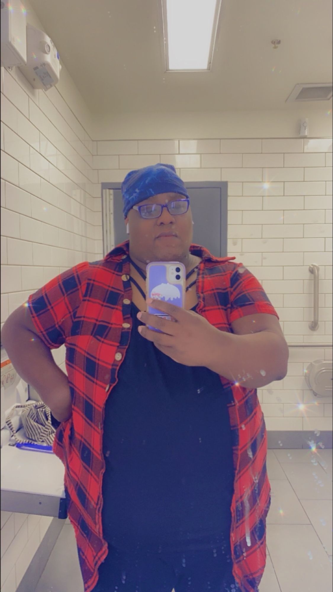 Synn standing in front of a retail store bathroom mirror with excellent lighting. She’s wearing a black and red shirt with black leggings.