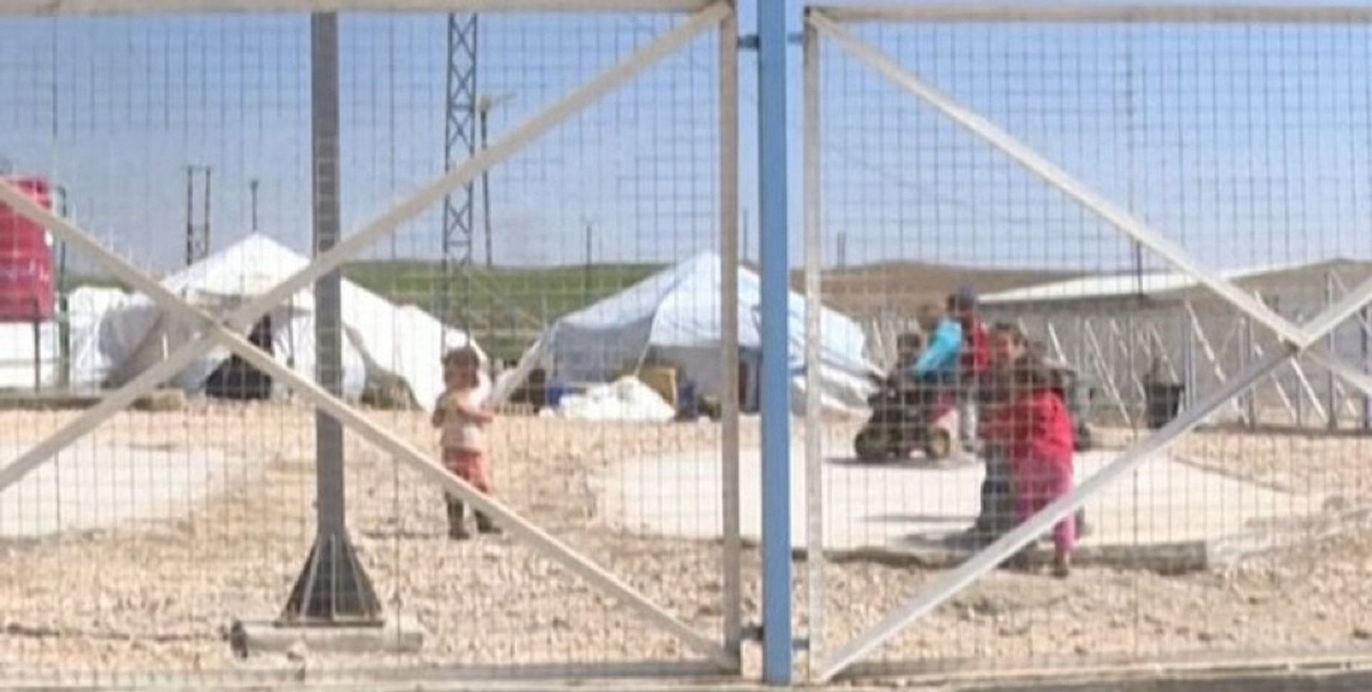 Des enfants derrière les grilles d’un camp.